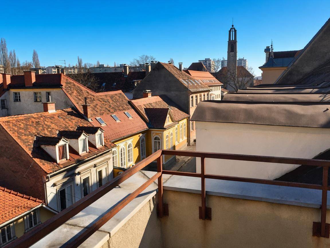 Panoramablick über die Dächer einer historischen Stadt mit einem markanten Kirchturm im Hintergrund.