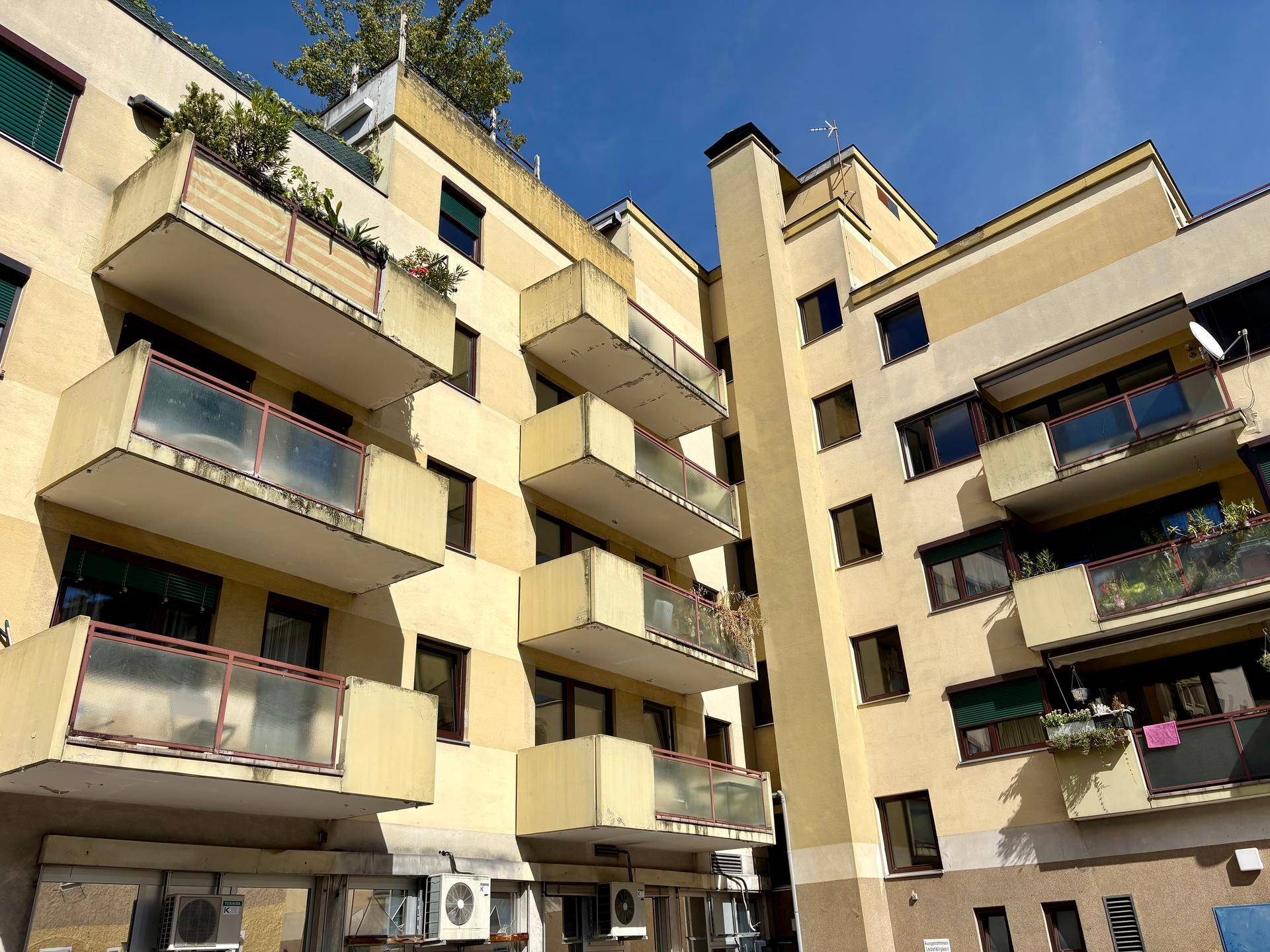 Mehrstöckiges Wohngebäude mit zahlreichen Balkonen und einer gelblichen Fassade unter blauem Himmel.