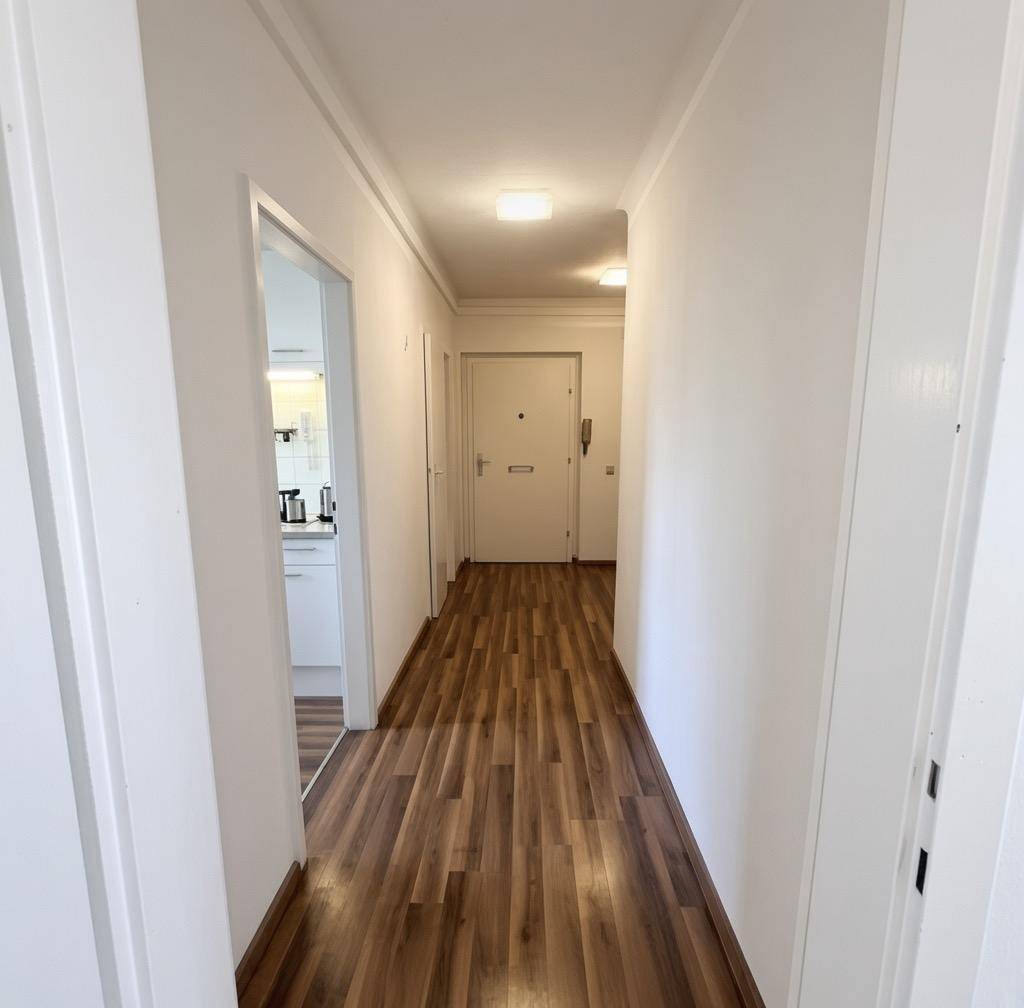 Heller Flur mit Laminatboden und weißen Wänden, der zu den verschiedenen Räumen der Wohnung führt.