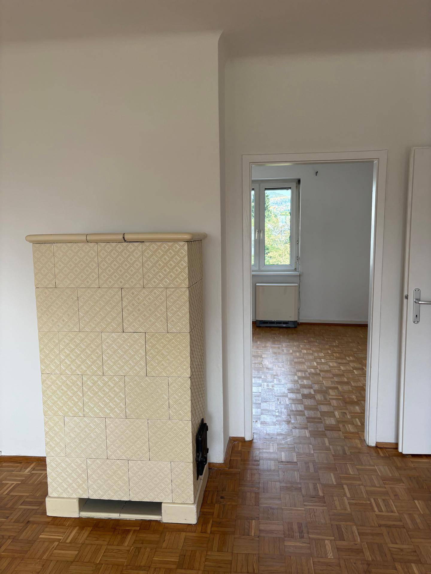 Traditioneller Kachelofen in einem hellen Raum mit Parkettboden, der Wärme und Gemütlichkeit spendet.