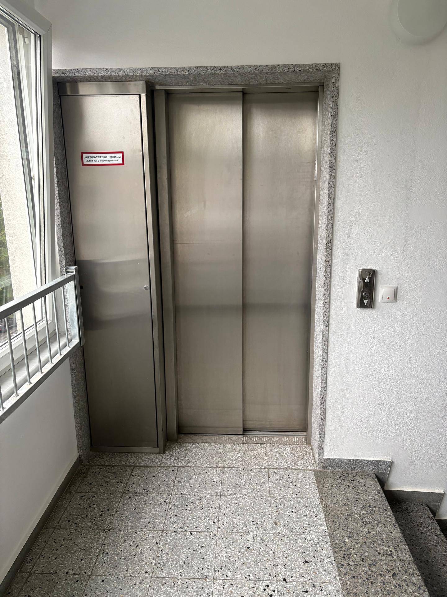 Moderner Aufzug mit Edelstahltüren und gefliestem Boden im Treppenhaus des Gebäudes.