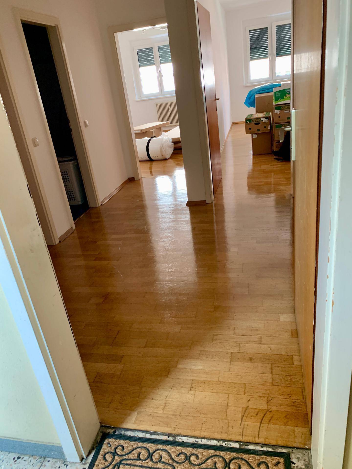 Heller Flur mit glänzendem Parkettboden, der zu verschiedenen Zimmern der Wohnung führt.