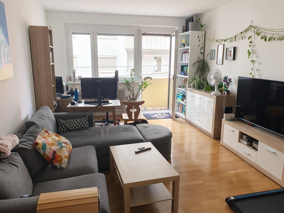 Gemütliches Wohnzimmer mit Sofa, Schreibtischbereich, Holzfußboden und direktem Zugang zum Balkon.