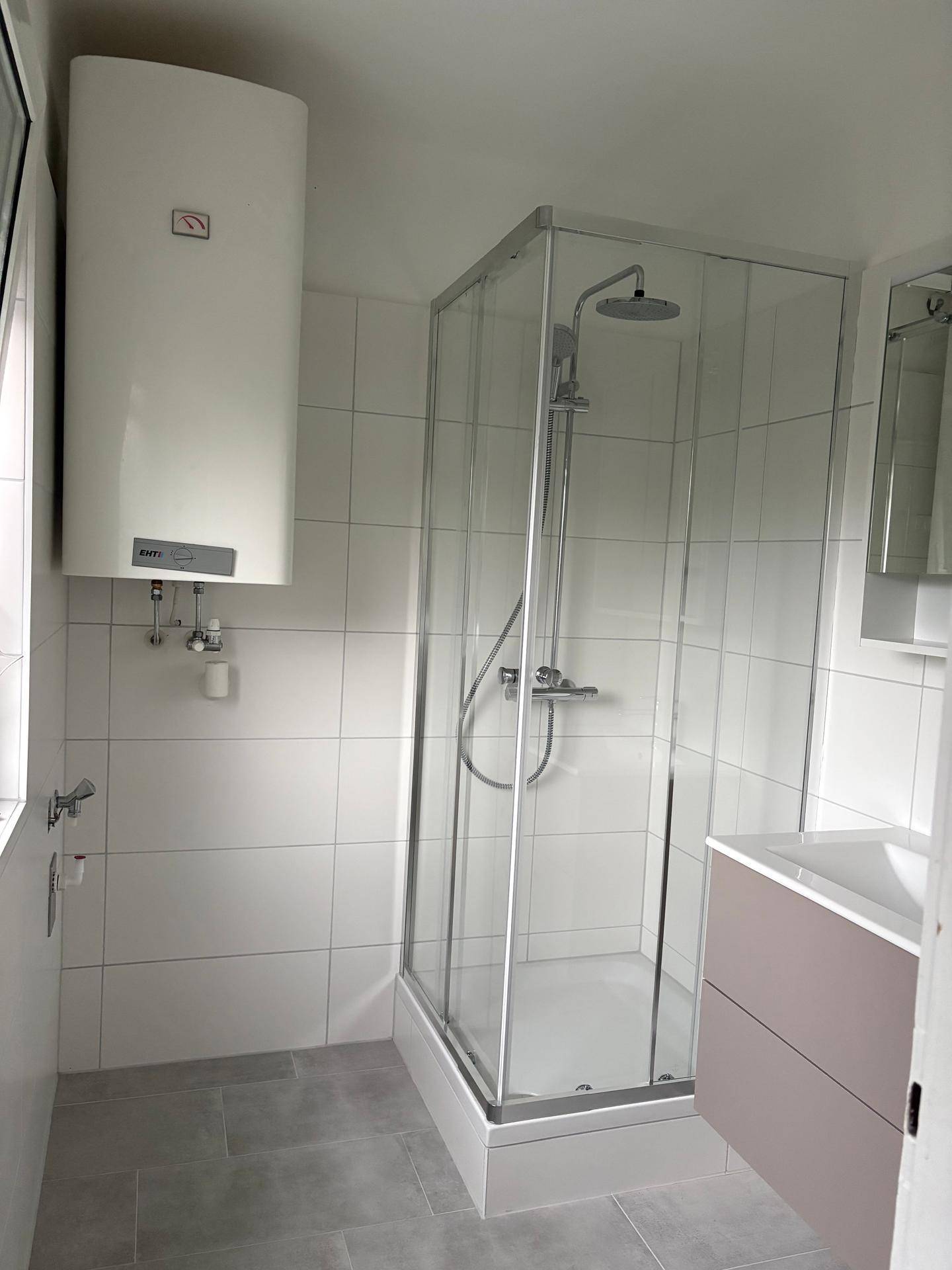 Modernes Badezimmer mit Duschkabine, Waschbecken mit Unterschrank und weiß-grauen Fliesen.
