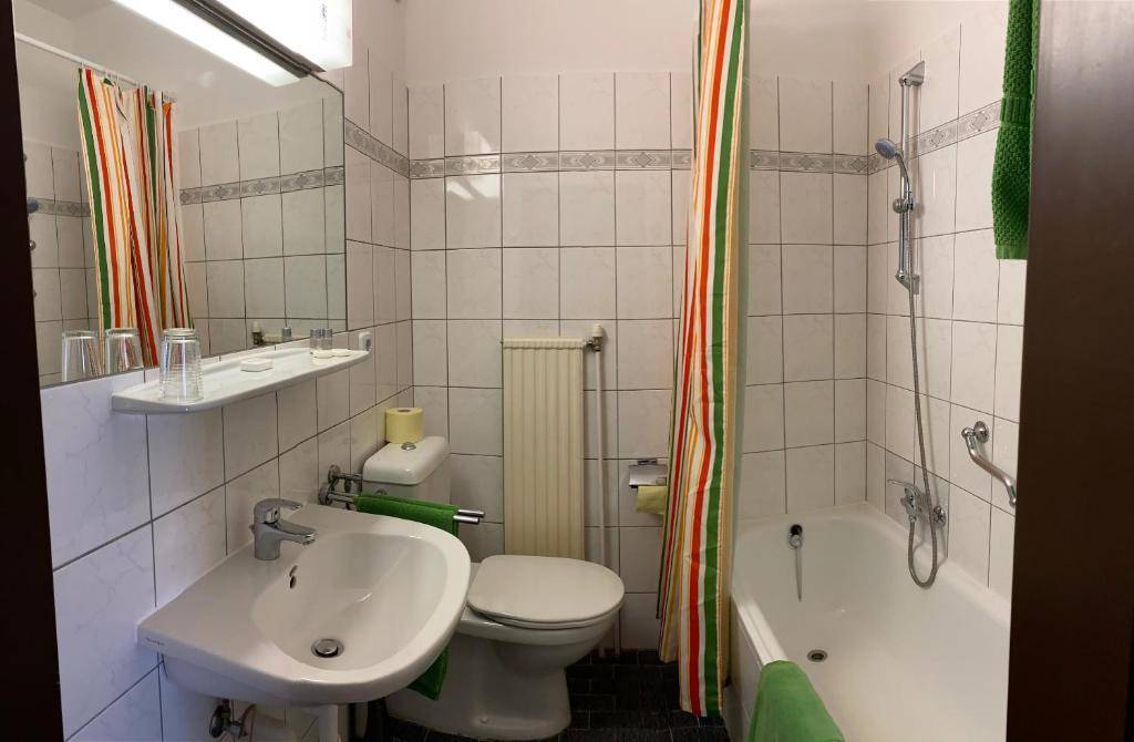 Funktionales Badezimmer mit Badewanne, WC, Waschbecken und weißen Fliesen, ausgestattet mit einem Duschvorhang.