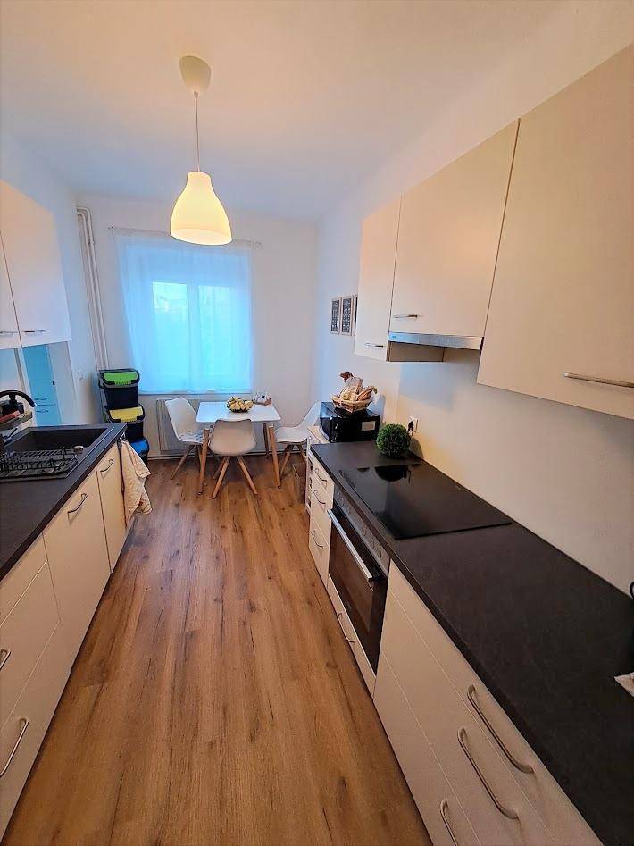 Funktionale Küche mit hellen Schränken, dunkler Arbeitsplatte und Essbereich am Fenster.