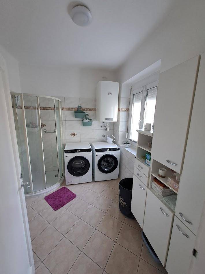 Badezimmer mit Duschkabine, Waschmaschinen und einem Fenster für Tageslicht.