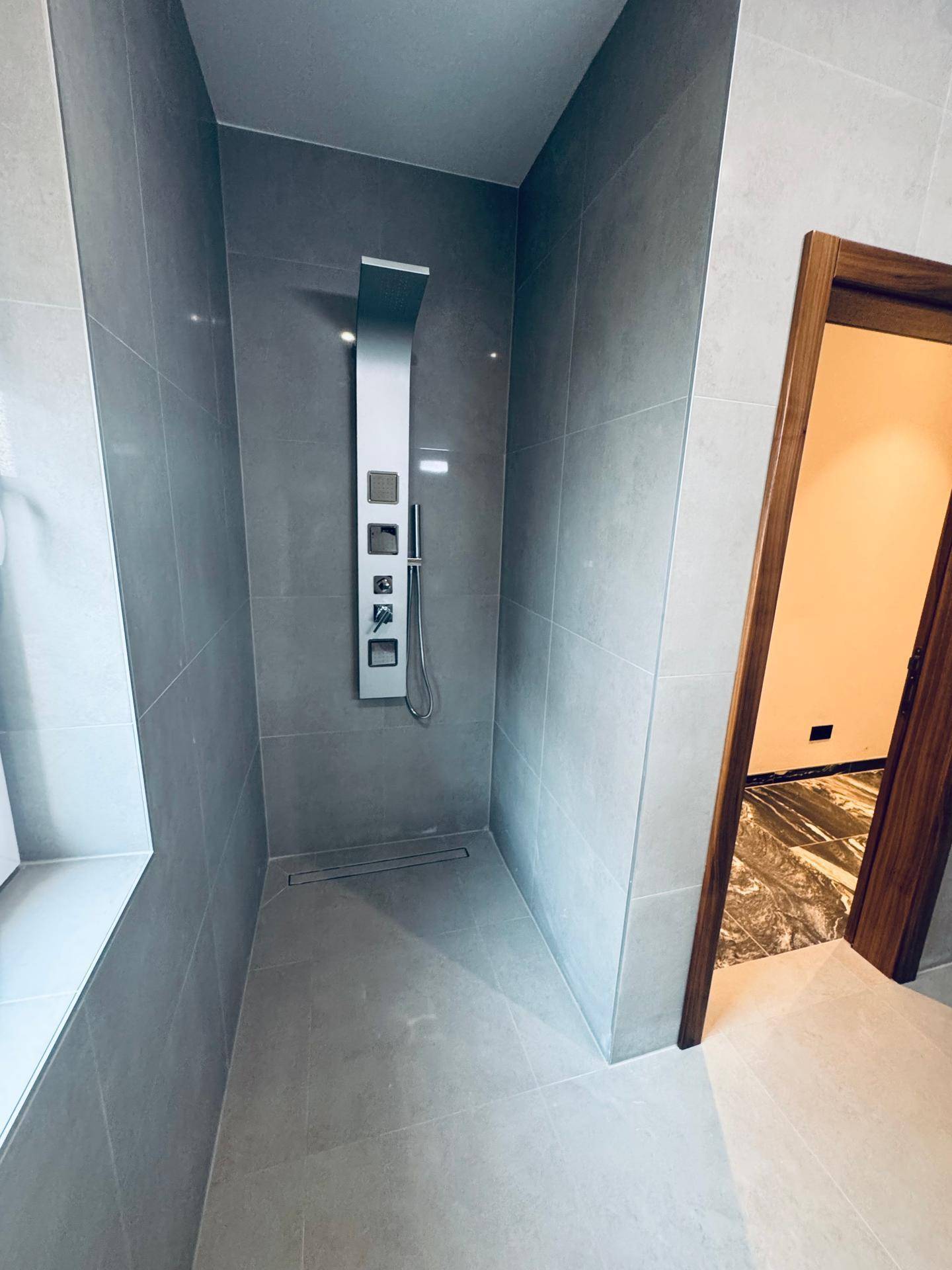 Moderne begehbare Dusche mit elegantem Duschpaneel und großformatigen grauen Fliesen.
