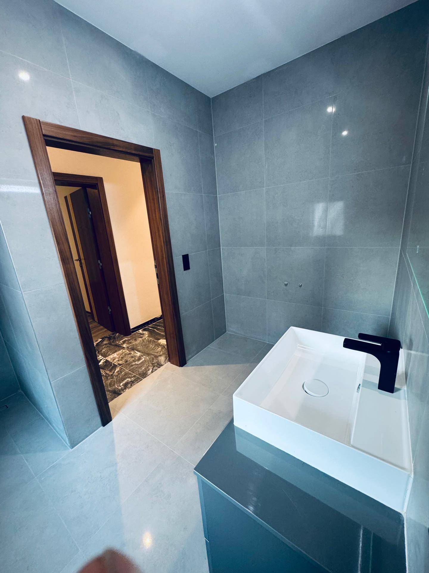 Modernes Badezimmer mit rechteckigem Aufsatzwaschbecken, dunklem Unterschrank und grauen Wandfliesen.