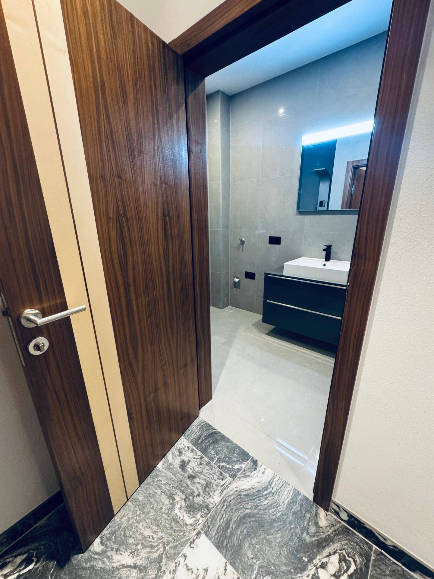 Blick in ein modernes Badezimmer mit grau gefliesten Wänden und Boden sowie einem stilvollen Waschtisch.