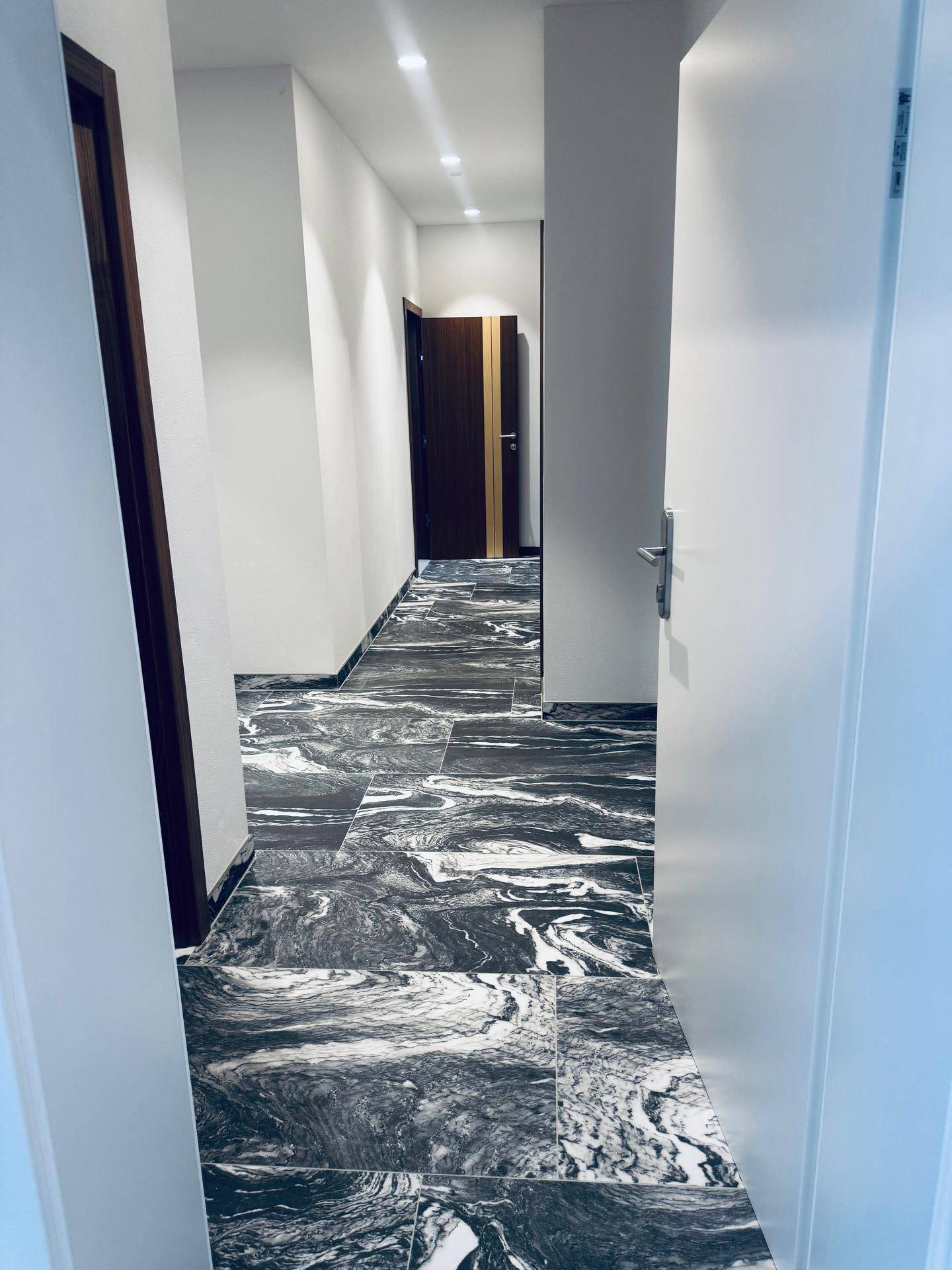 Langer, heller Flur mit auffälligem schwarz-weißem Marmorfliesenboden und modernen Holztüren.
