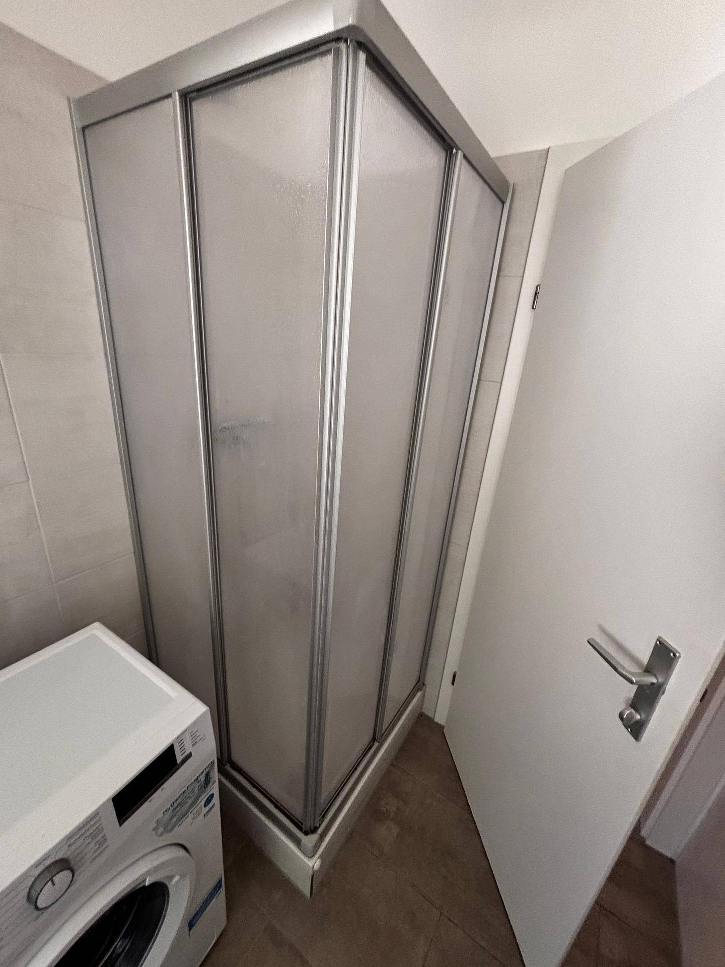 Duschkabine mit Milchglas und Waschmaschine im Badezimmer.
