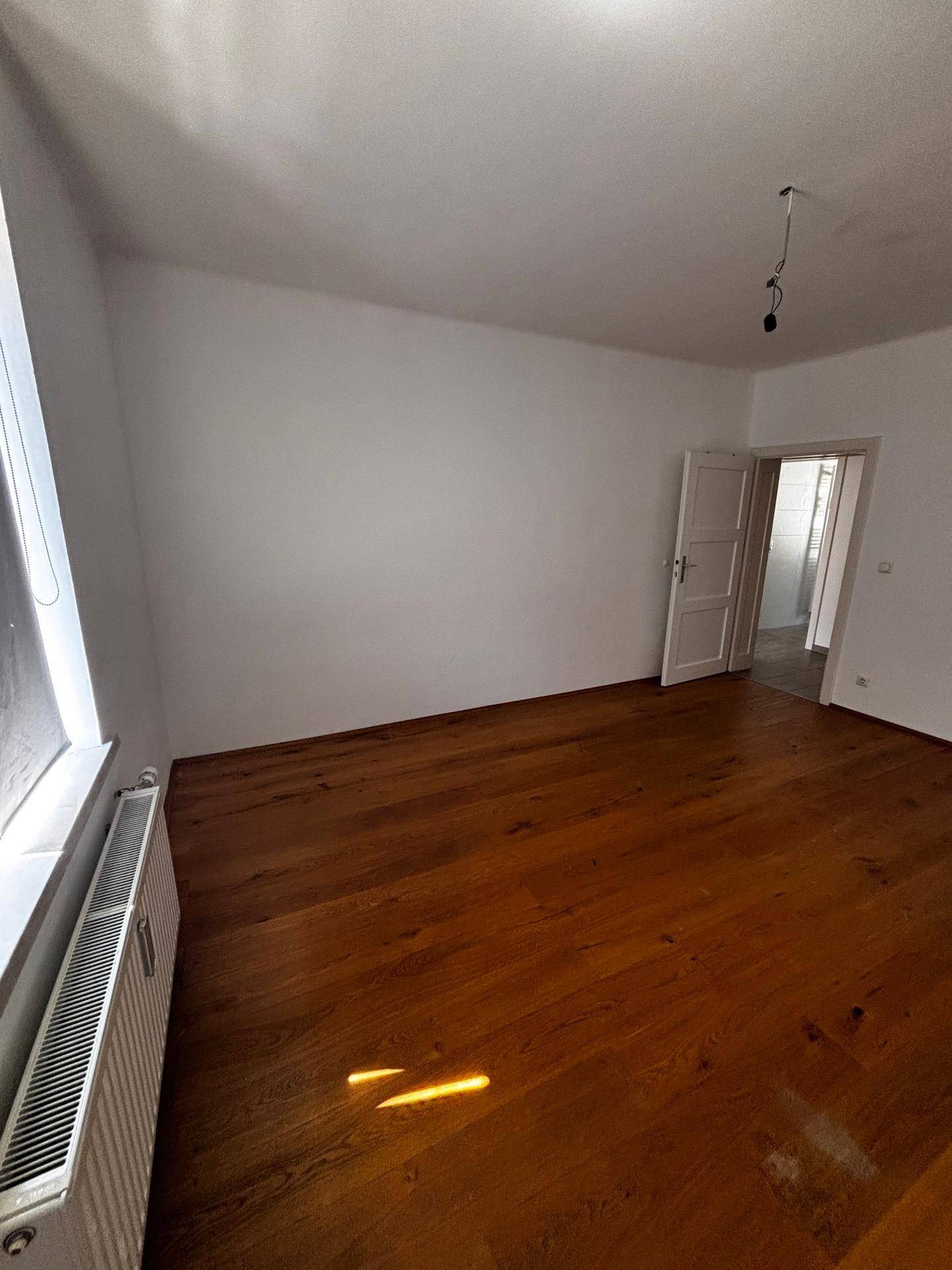 Helles Zimmer mit Holzboden, Fenster und Heizkörper, ideal für Schlaf- oder Arbeitszimmer.