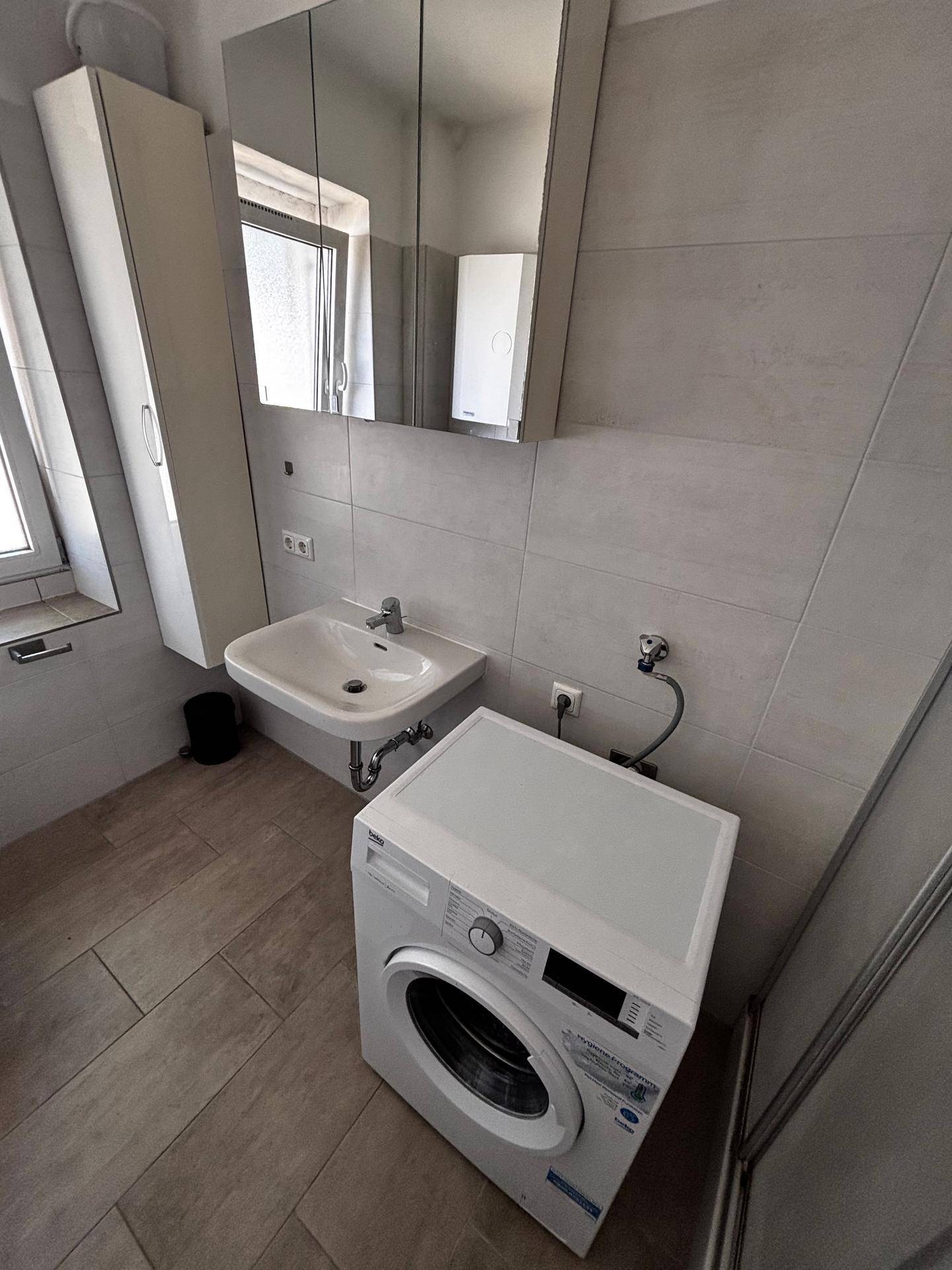 Badezimmer mit Waschbecken, Spiegelschrank, Waschmaschine und Fenster.