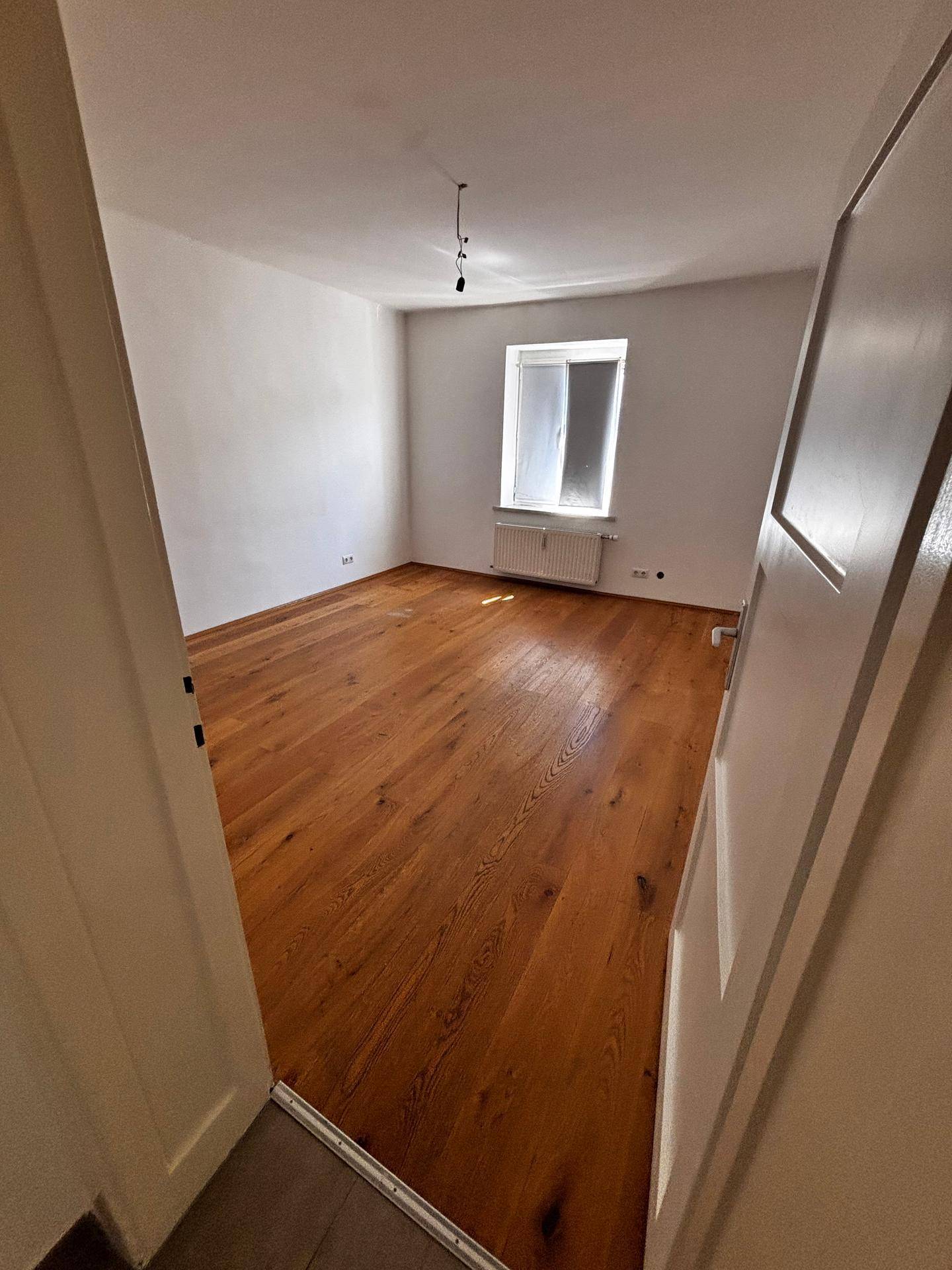 Helles, leeres Zimmer mit Holzboden und Fenster, bereit für neue Bewohner.