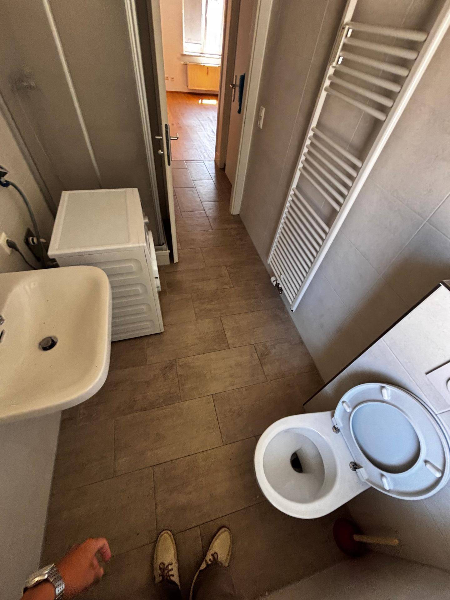 Badezimmer mit Toilette, Waschbecken, Waschmaschine, Handtuchheizkörper und Duschkabine.