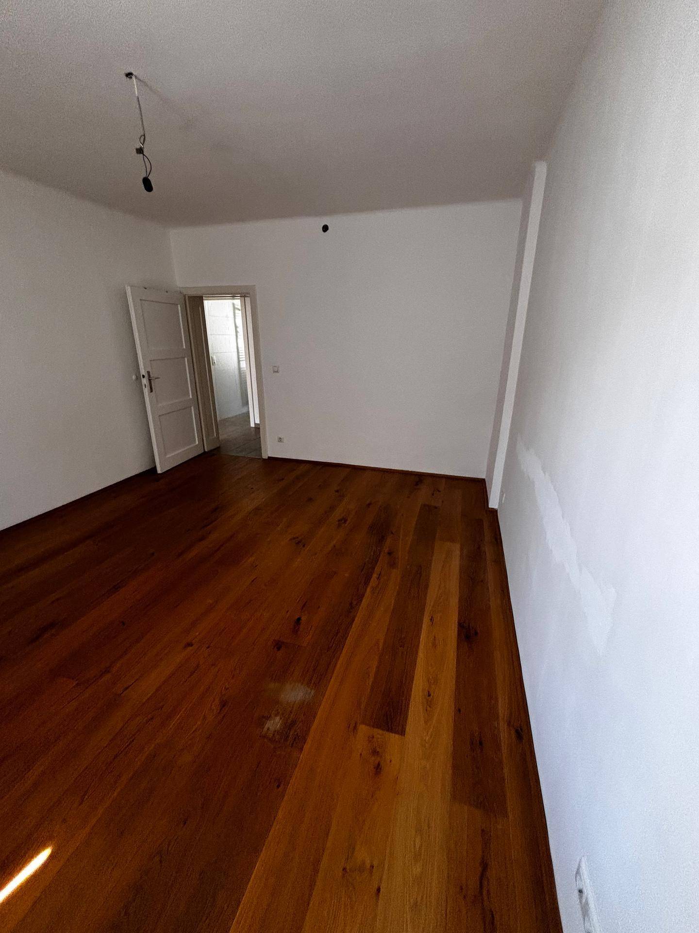 Geräumiges, leeres Zimmer mit Holzboden und weiß gestrichenen Wänden.