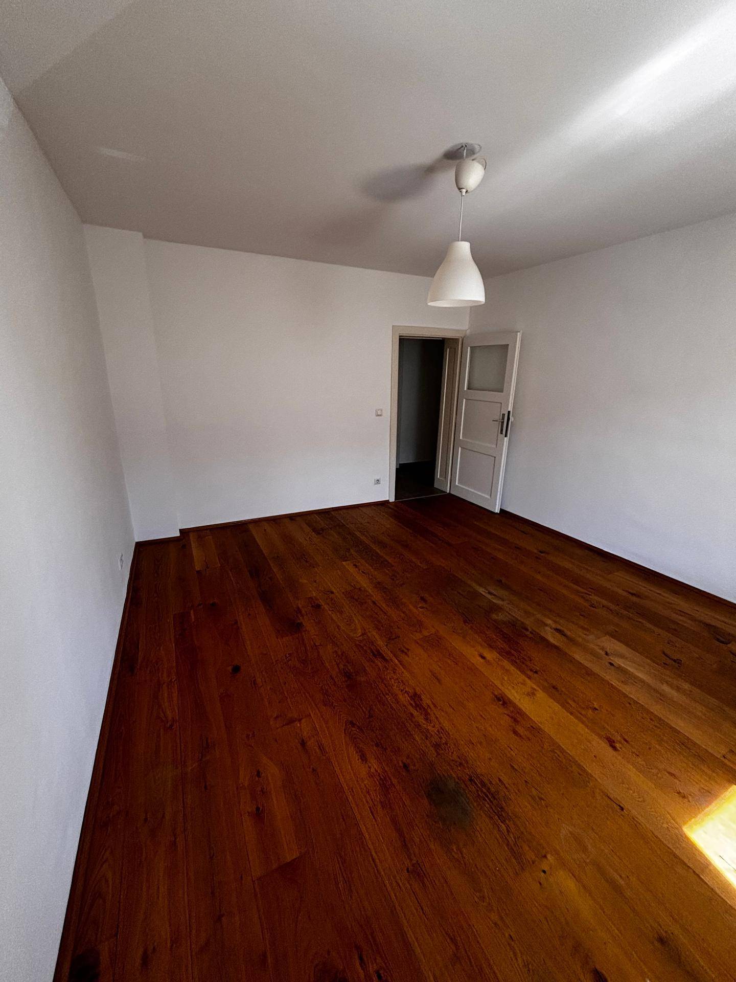 Geräumiges, leeres Zimmer mit glänzendem Holzboden und Zugang zu einem weiteren Raum.