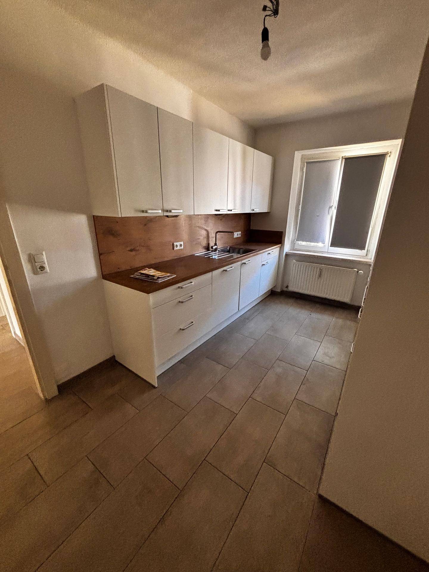 Helle Küche mit weißen Oberschränken, Holzarbeitsplatte, Spüle und Fenster.