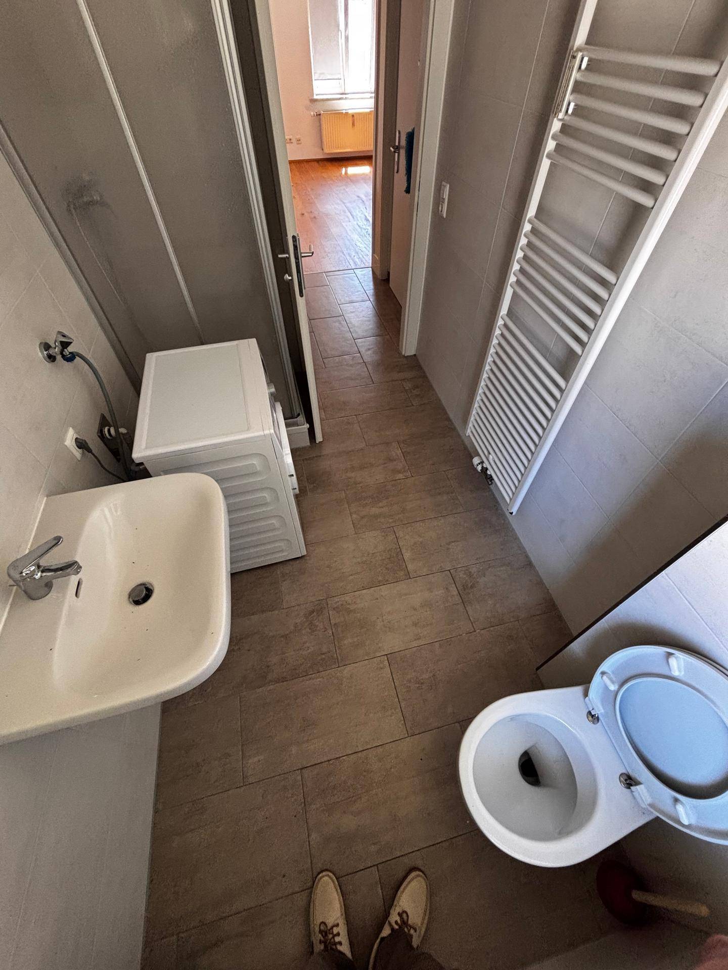 Funktionales Badezimmer mit Waschbecken, Toilette, Waschmaschine und Duschkabine.