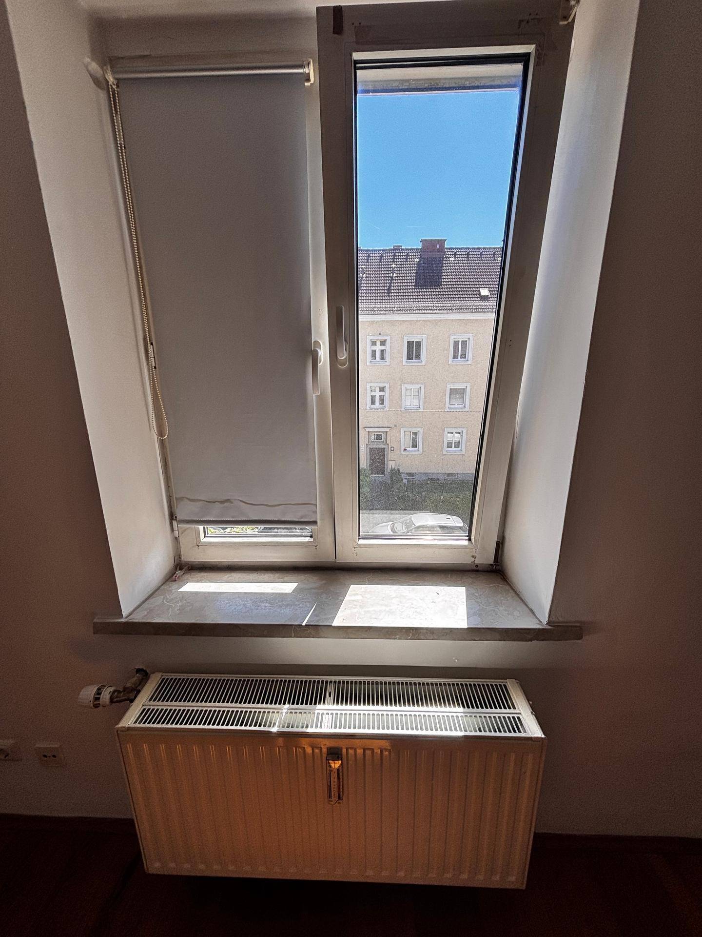 Fenster mit Blick auf ein gegenüberliegendes Gebäude und einem Heizkörper darunter.