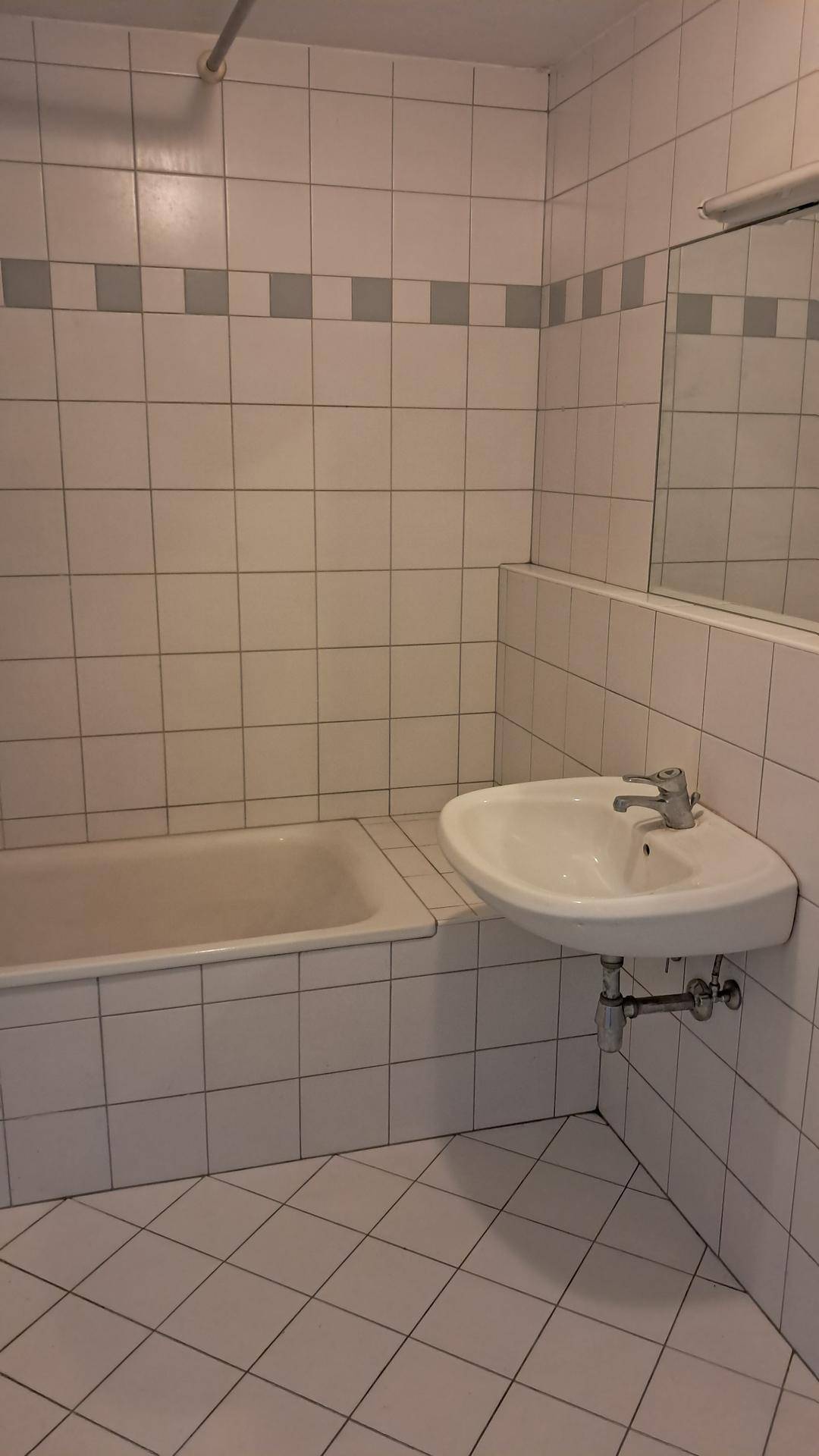 Badezimmer mit Badewanne, Waschbecken und weißen Fliesen, in gutem Zustand.