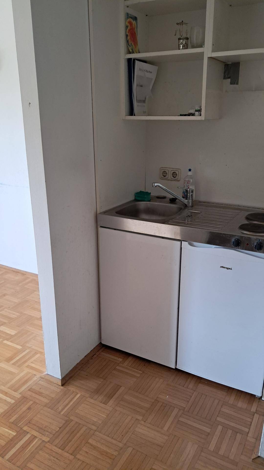 Kleine Küchenzeile mit Spüle, Kochfeld und Kühlschrank, ideal für kompaktes Wohnen.
