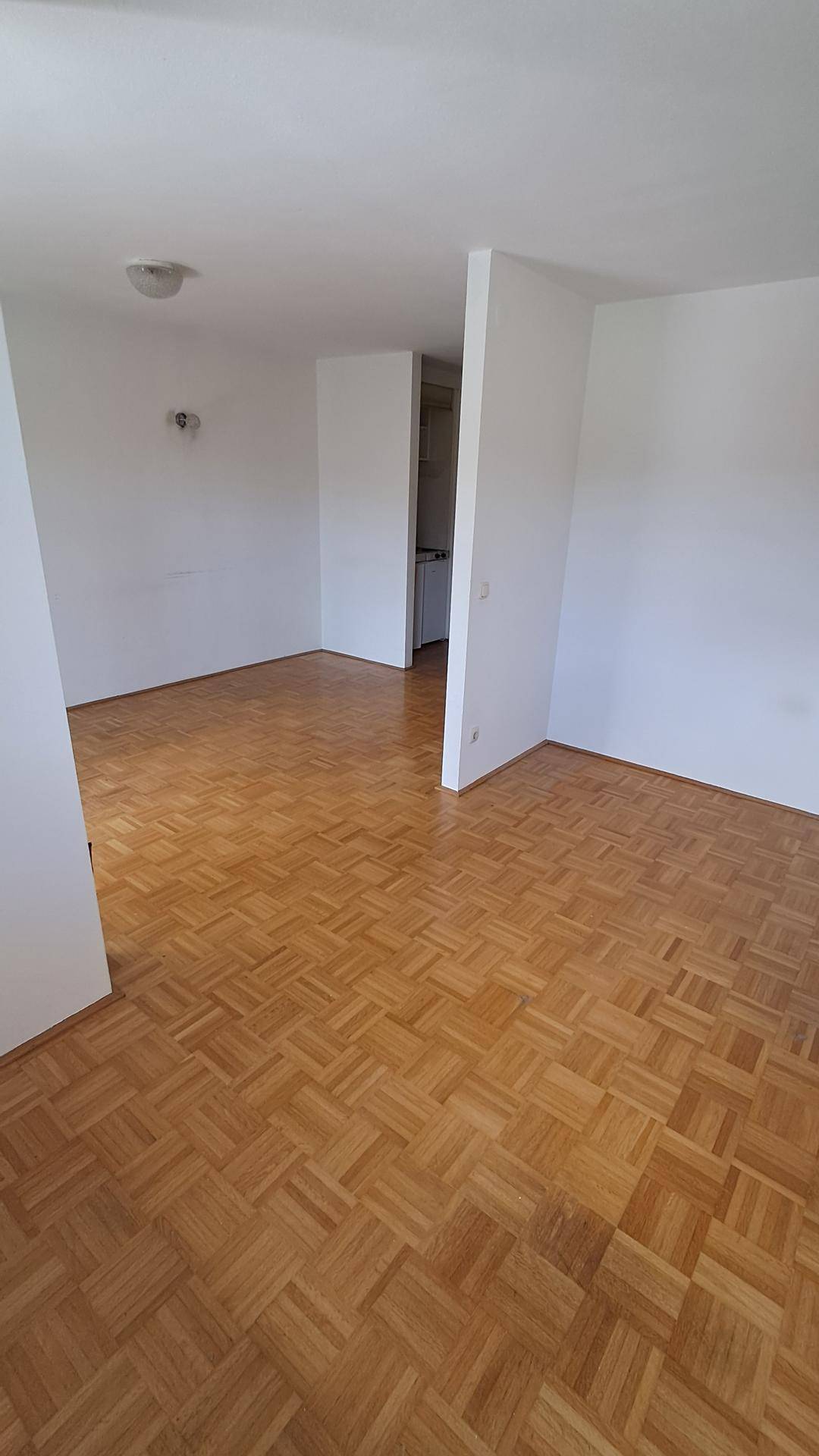 Geräumiger, heller Raum mit Parkettboden und Zugang zu einem weiteren Bereich.