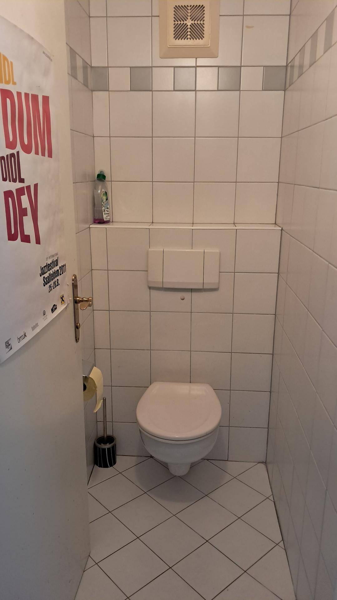 Kleines WC mit wandhängender Toilette, weißen Fliesen und Lüftungssystem.