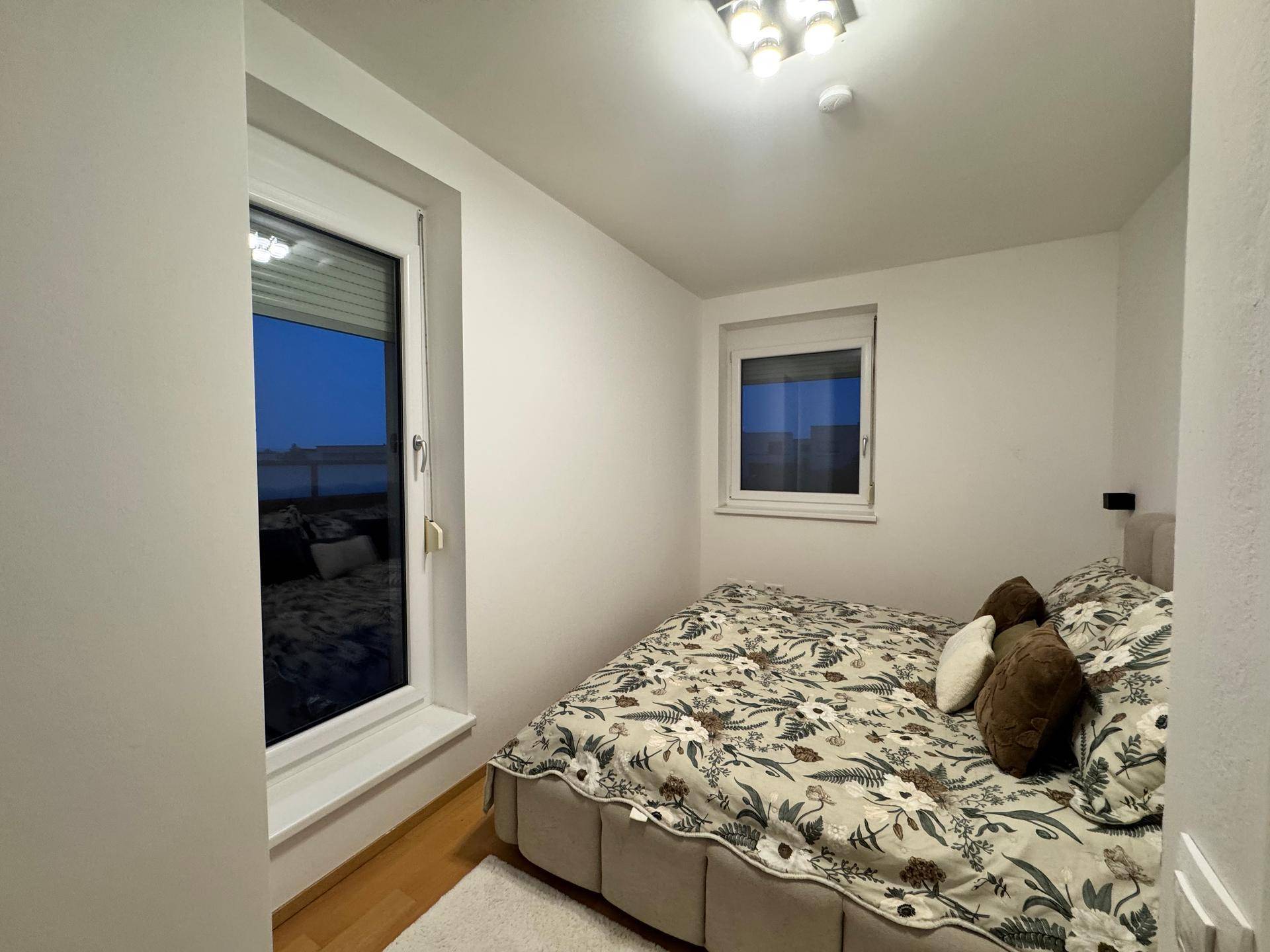 Gemütliches Schlafzimmer mit zwei Fenstern, Holzboden und schlichter Einrichtung.