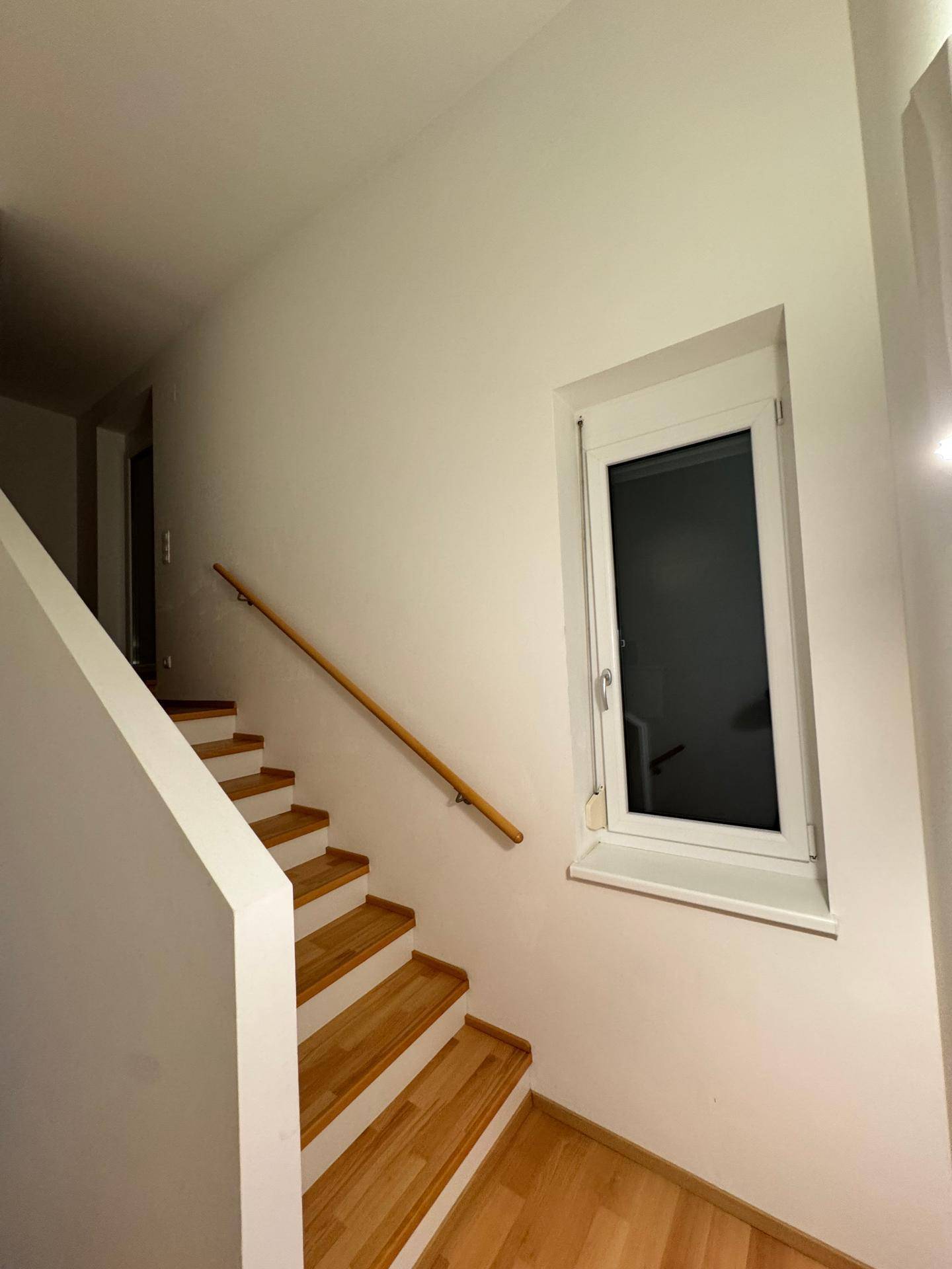 Treppenhaus mit Holzstufen, Handlauf und einem Fenster für natürliches Licht.
