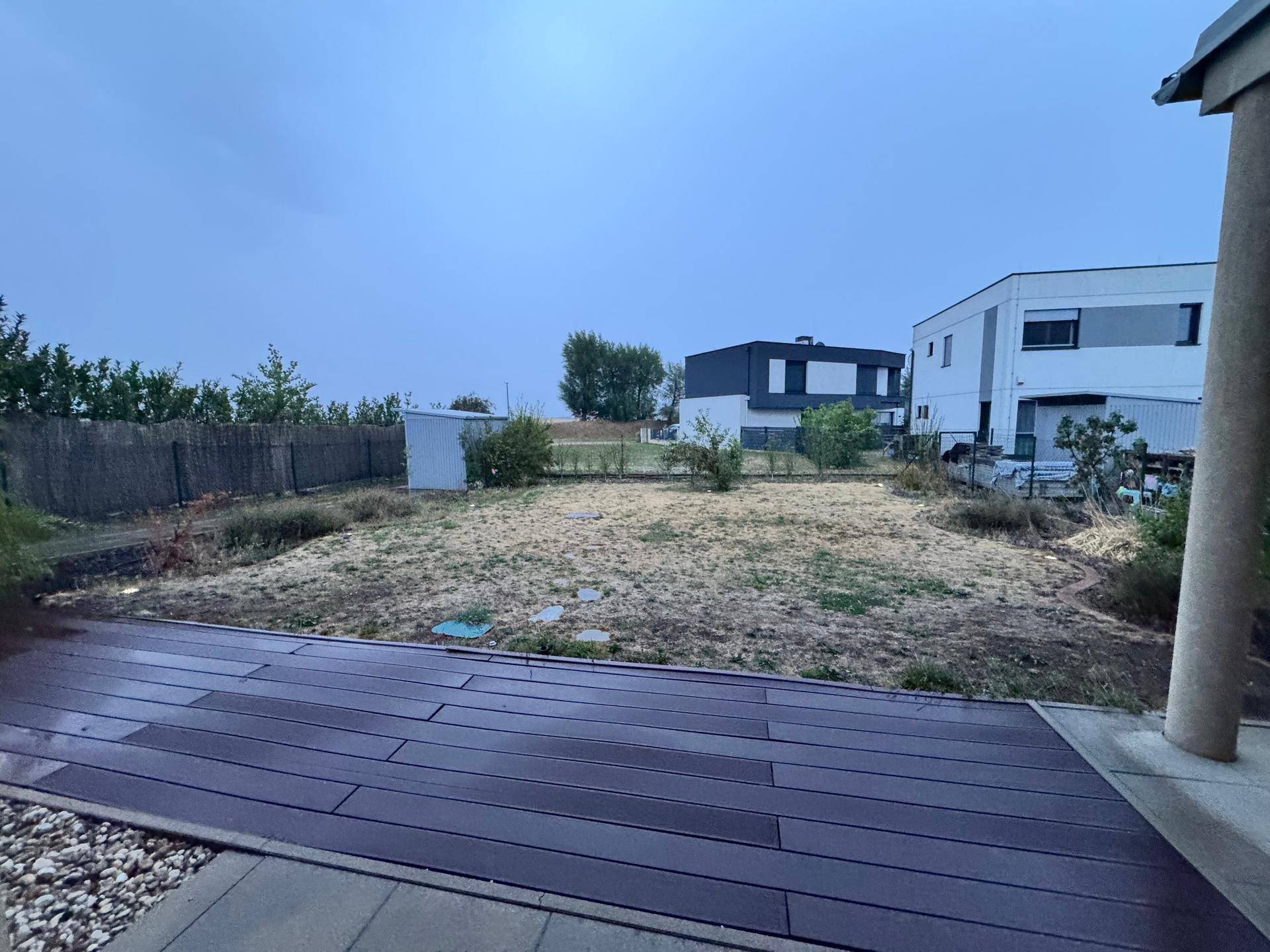 Großer Gartenbereich mit Holzterrasse und Blick auf benachbarte Häuser.