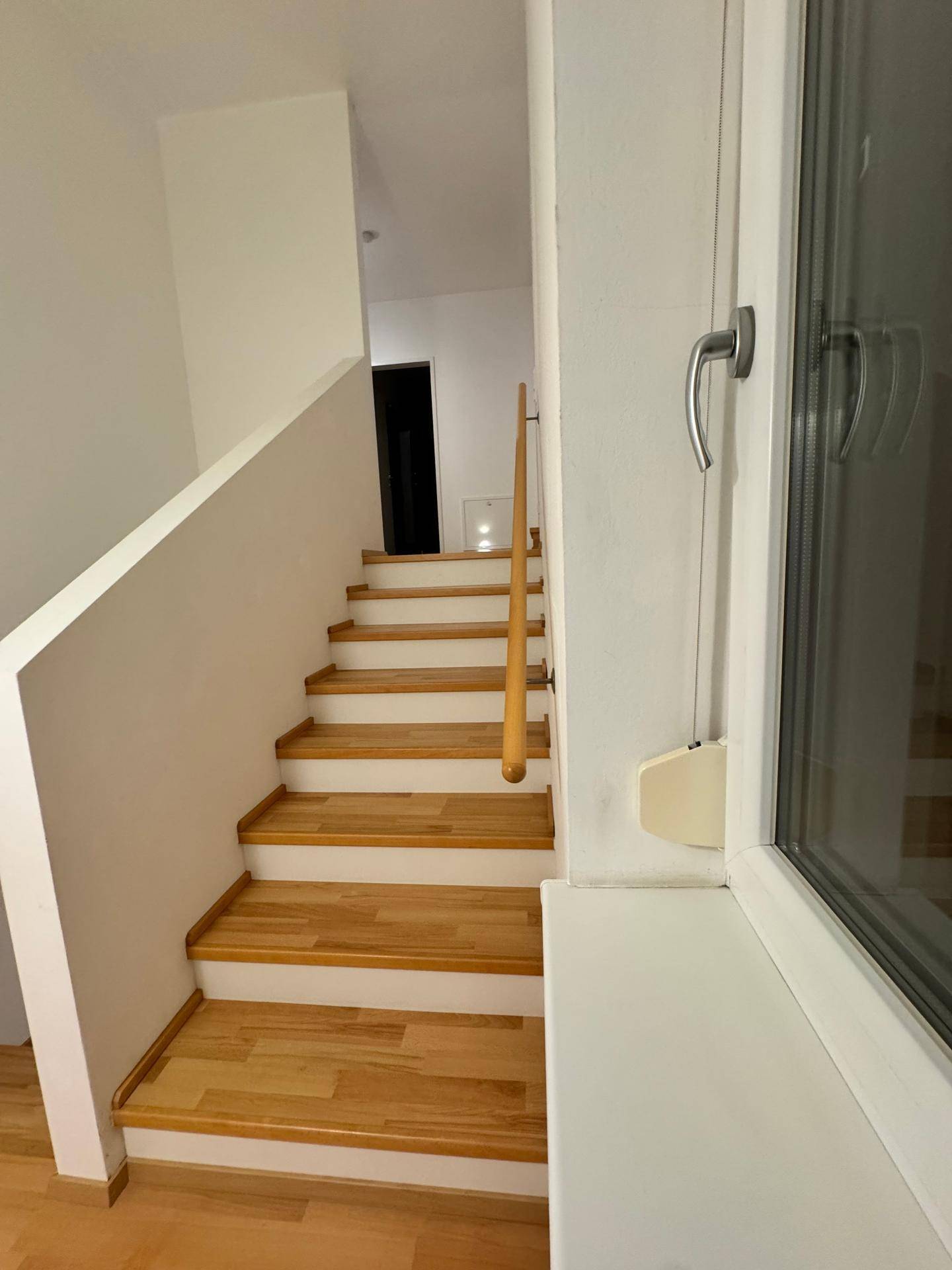 Heller Treppenaufgang mit Holzstufen und einem Fenster, das Tageslicht hereinlässt.
