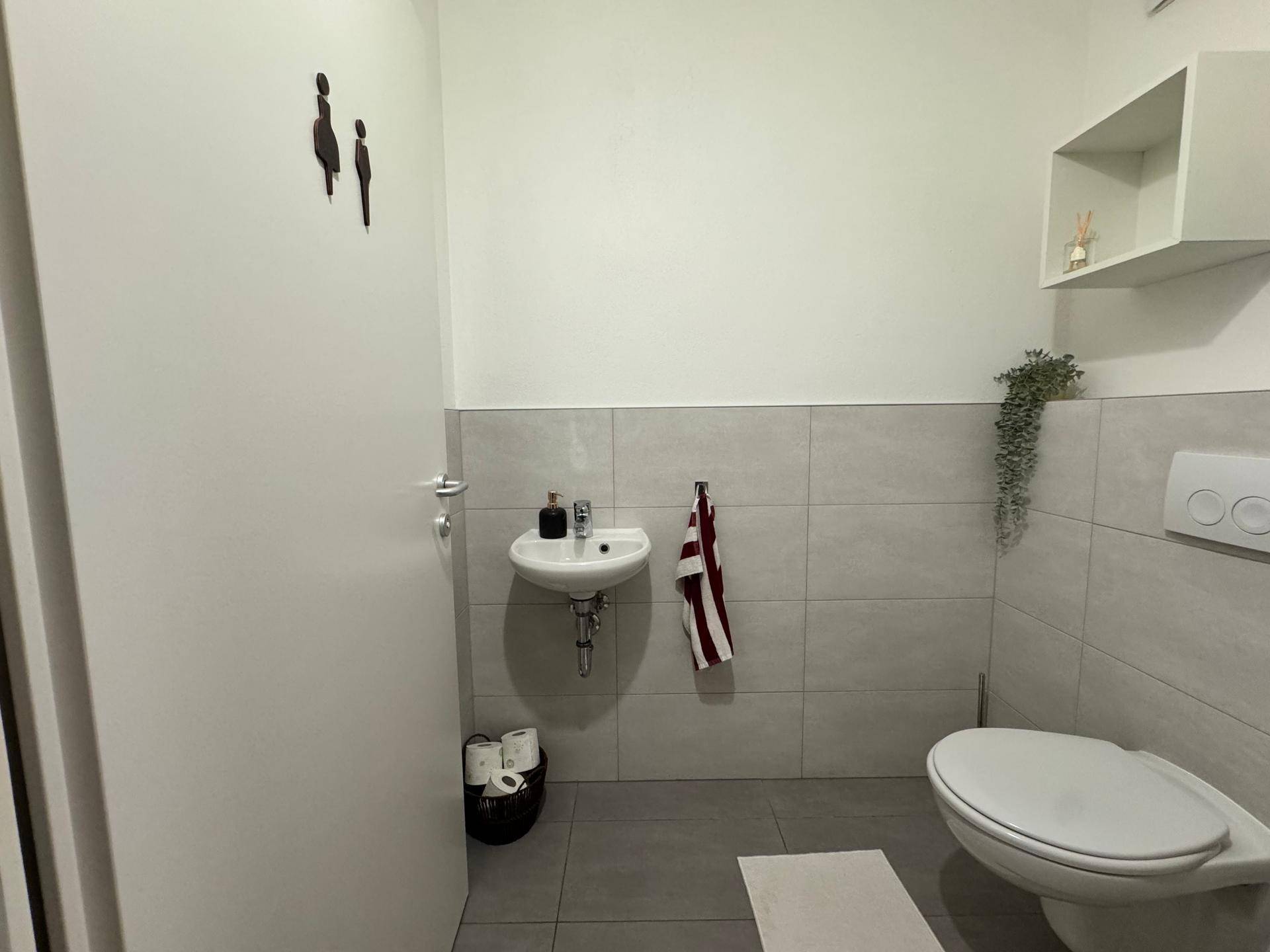 Helles Gäste-WC mit modernem Design, kleinem Waschbecken und grauen Wandfliesen.