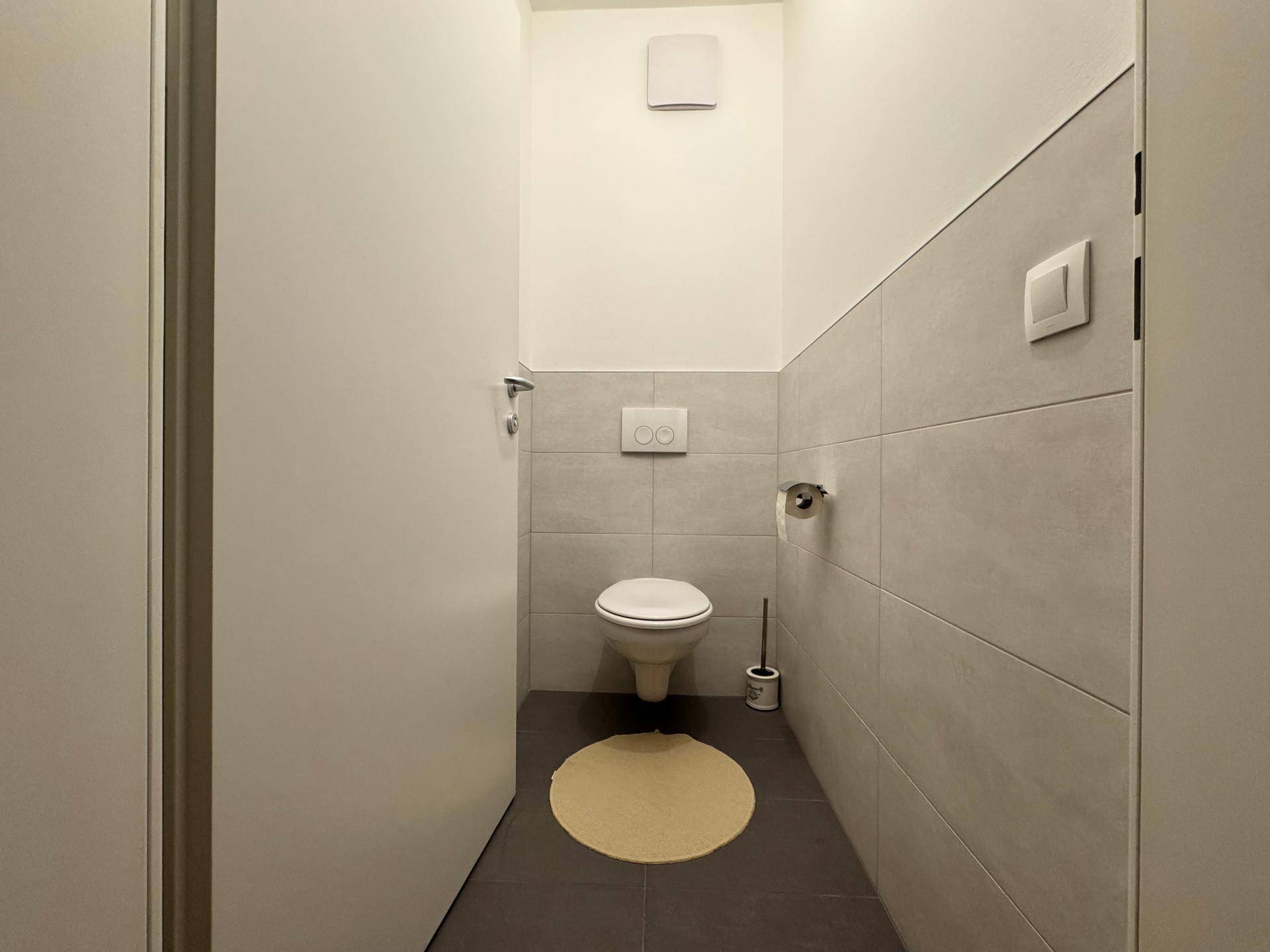Modernes Gäste-WC mit wandhängender Toilette und grauen Fliesen an Wänden und Boden.