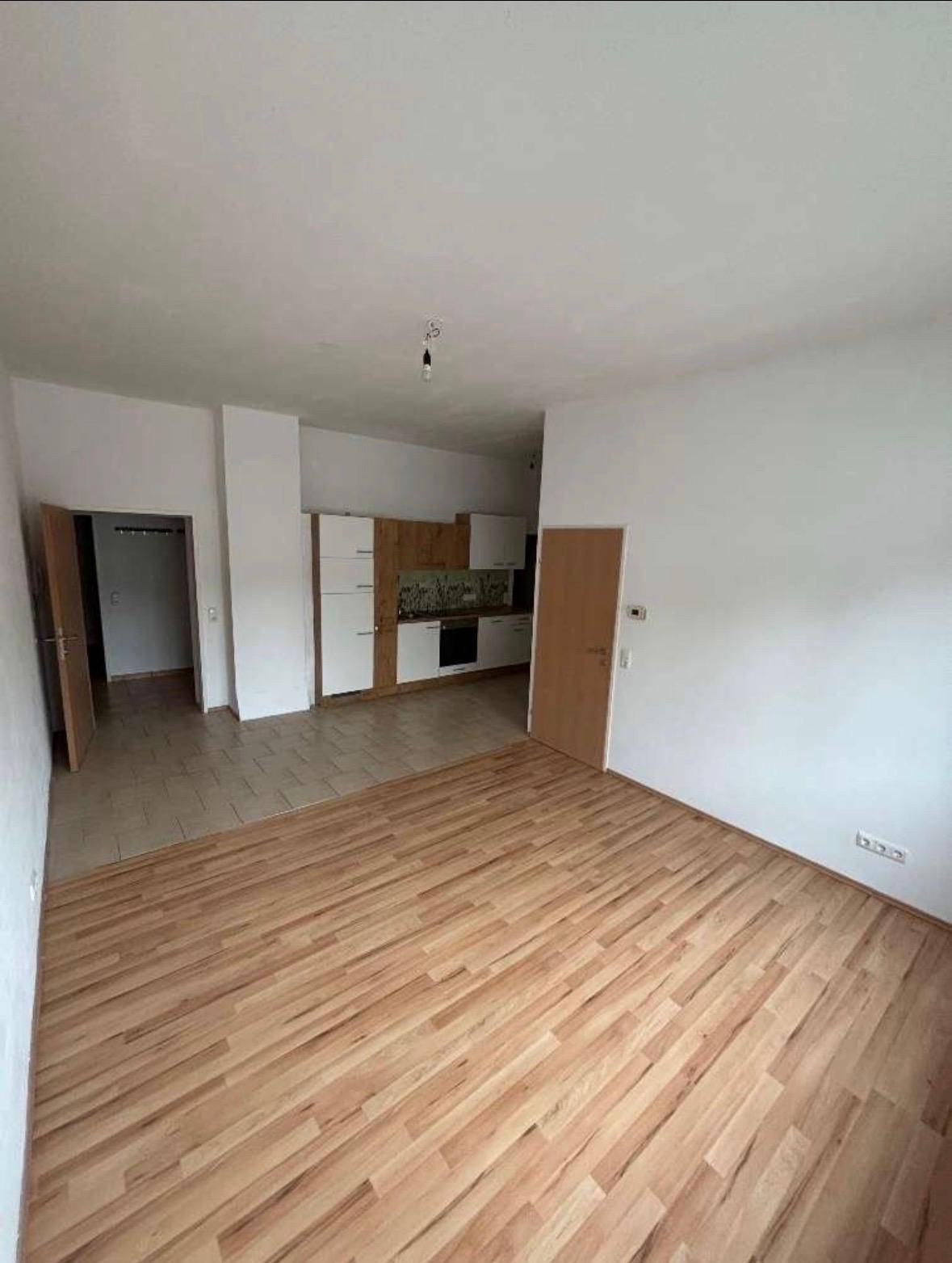 Offener Wohnbereich mit Holzboden, der in einen Küchenbereich mit hellen Schränken übergeht.