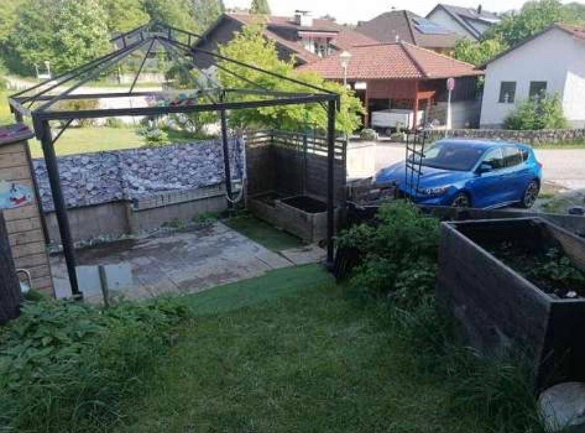 Gartenbereich mit Rasenfläche, gepflastertem Sitzplatz, einem Pavillon und Hochbeeten.