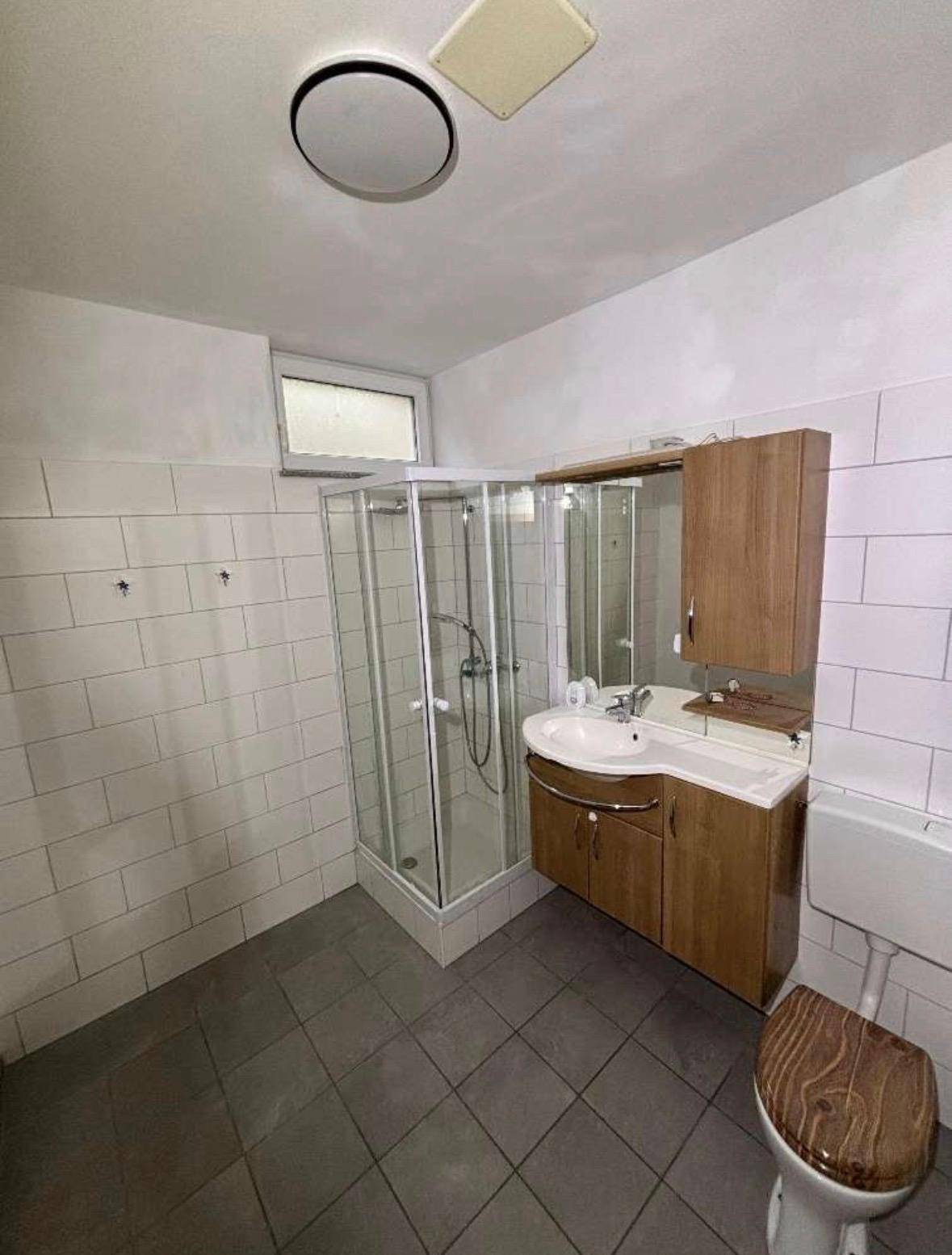Funktionales Badezimmer mit Duschkabine, Waschbecken und WC, ausgestattet mit Fliesen und Holzdetails.