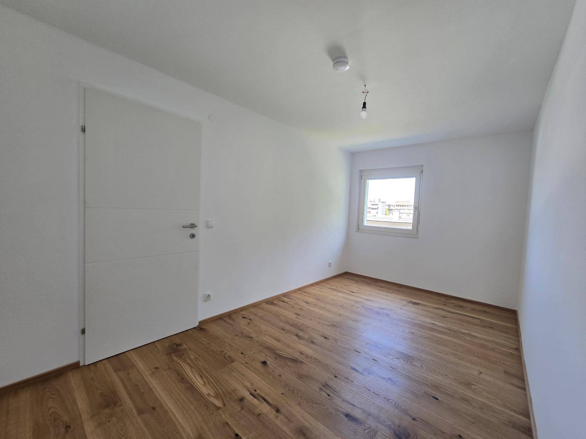 Ruhiges Schlafzimmer mit Holzboden und einem Fenster, das viel Tageslicht hereinlässt.