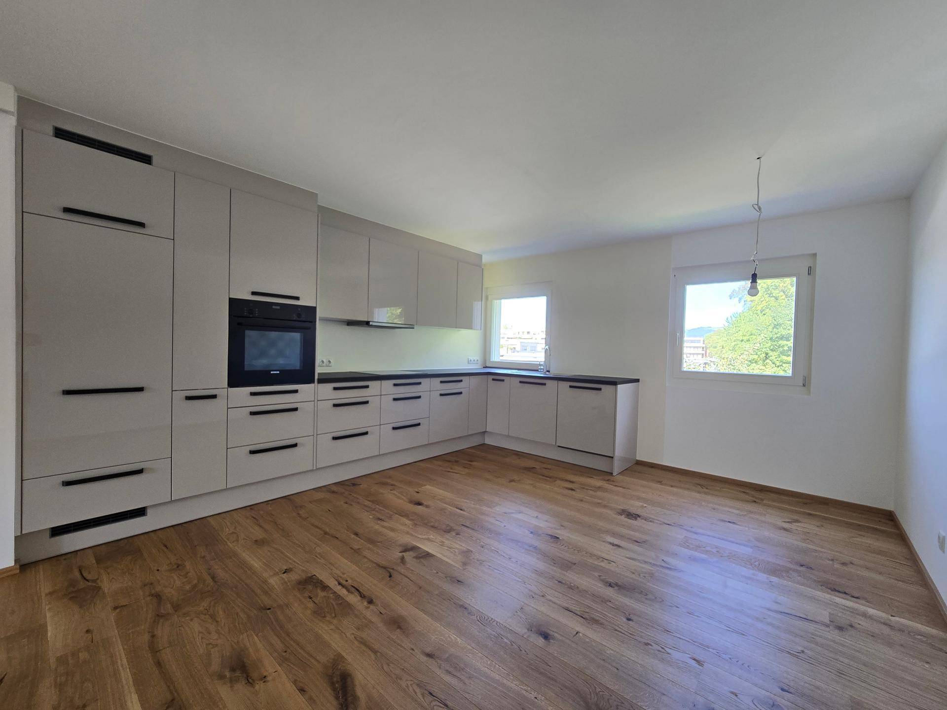 Moderne Einbauküche in hellem Grau mit integrierten Geräten und Holzparkettboden.