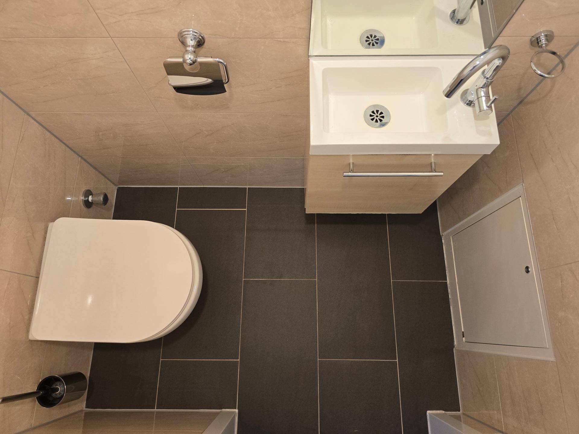 Separates Gäste-WC mit modernem Design, kleinem Waschbecken und dunklen Bodenfliesen.