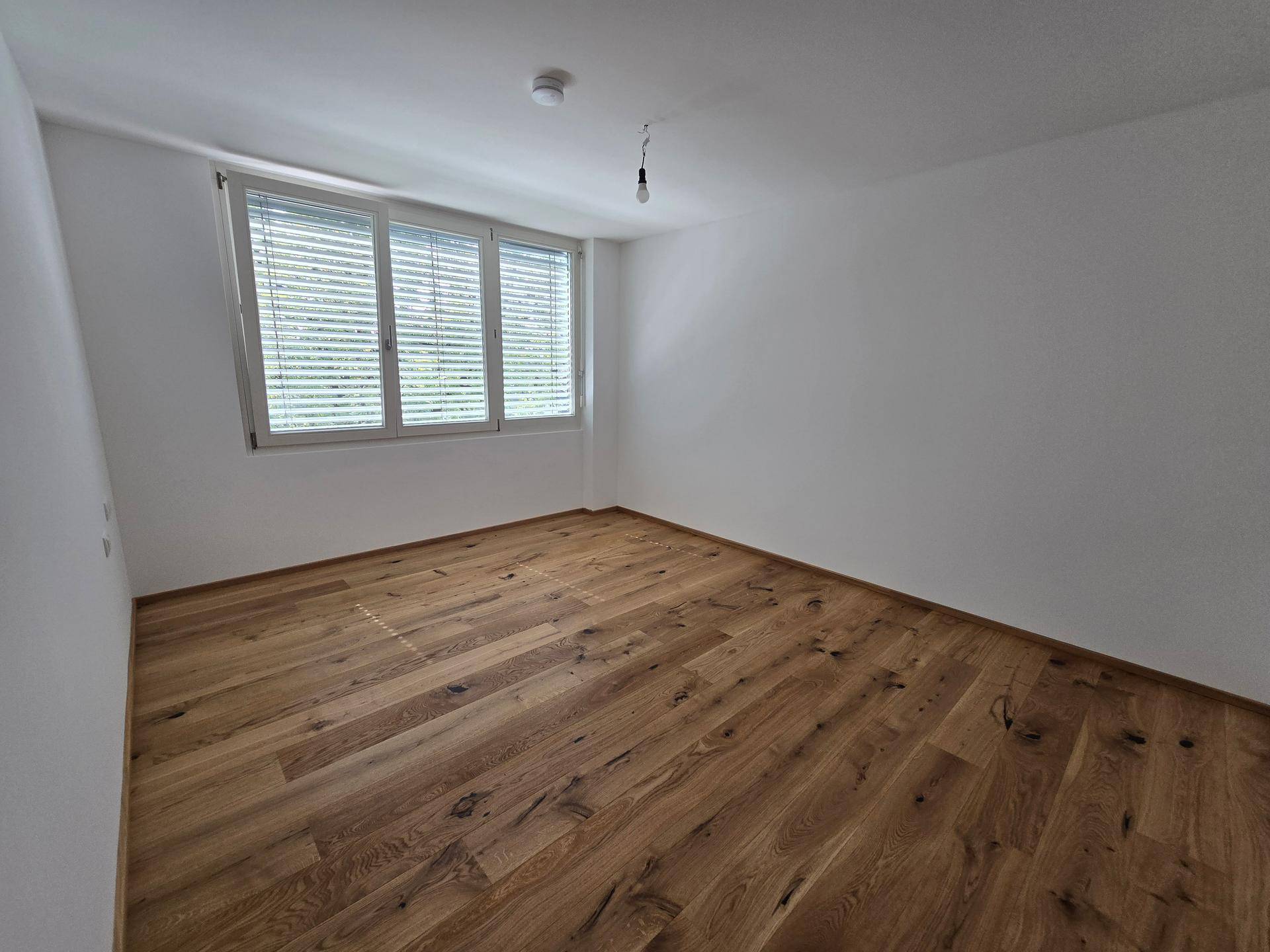 Geräumiges Schlafzimmer mit Parkettboden und breitem Fenster für optimale Belichtung.