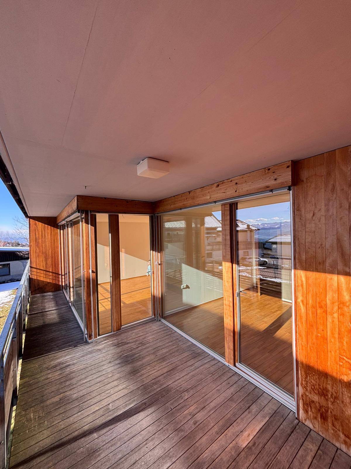 Geräumiger Balkon mit Holzbelag, Glasschiebetüren und Panoramablick auf die Berge.