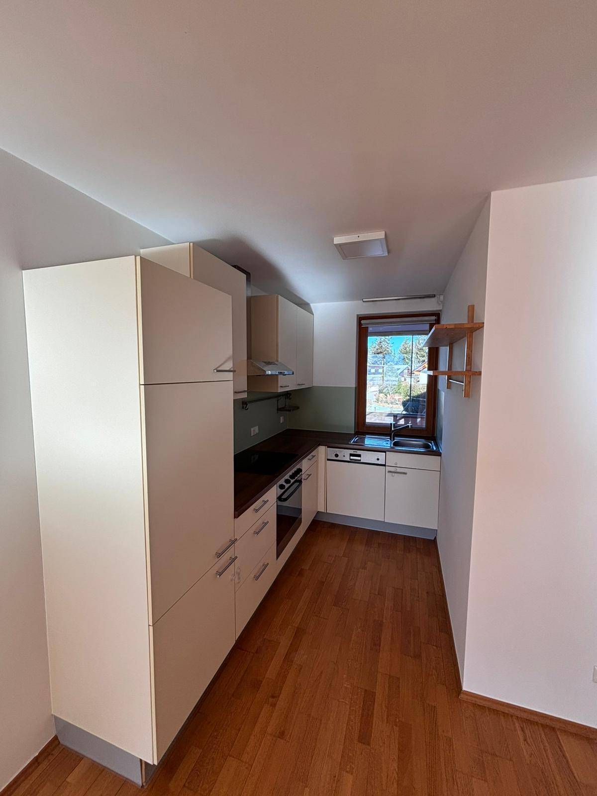 Schmale Küche mit hellen Einbauschränken, Holzfußboden und Fenster.