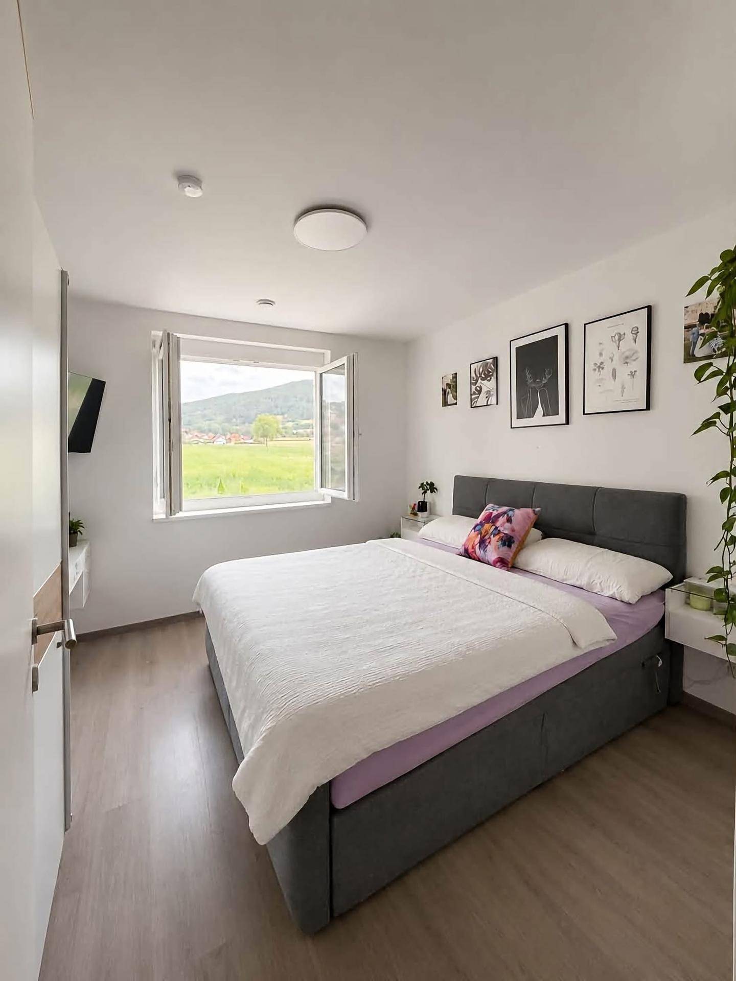 Helles Schlafzimmer mit Doppelbett, Laminatboden und weitem Blick ins Grüne.