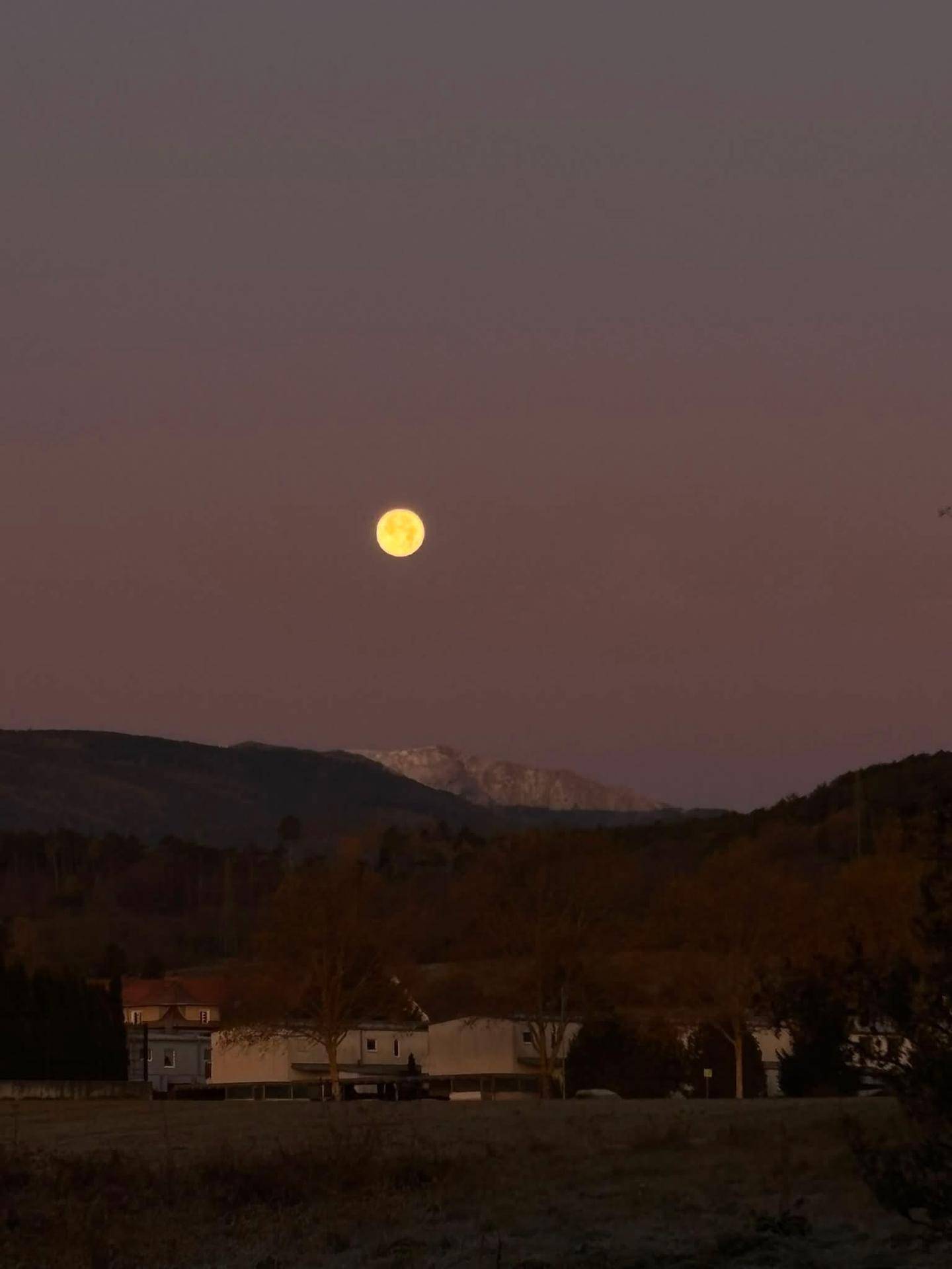 Vollmond über einer ruhigen ländlichen Landschaft mit dunklen Bergen im Hintergrund.