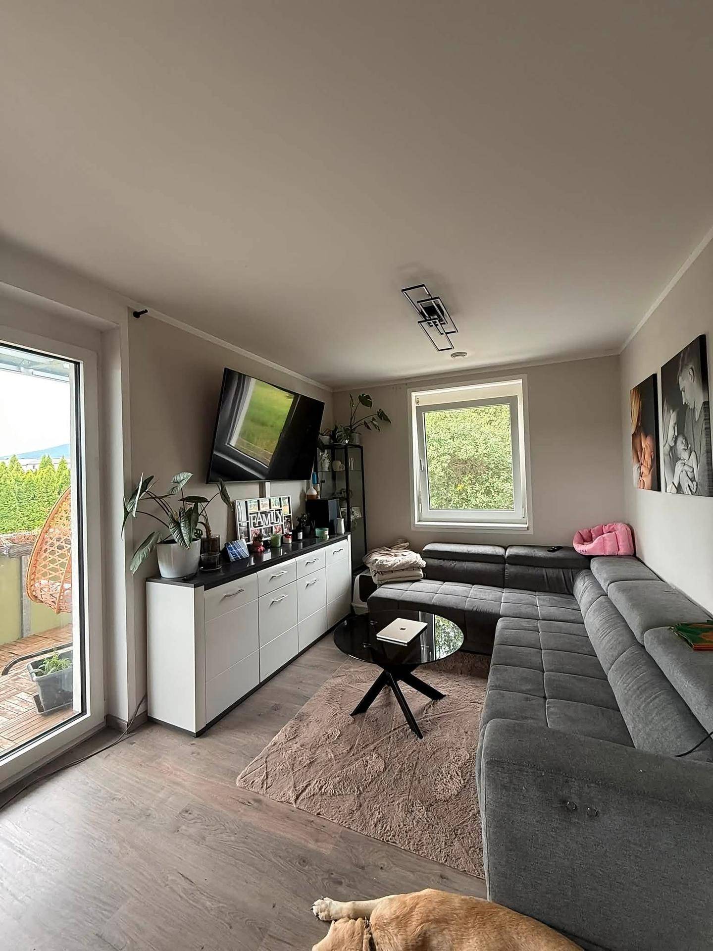 Gemütliches Wohnzimmer mit großem Ecksofa, Fernseher und Zugang zum Balkon.