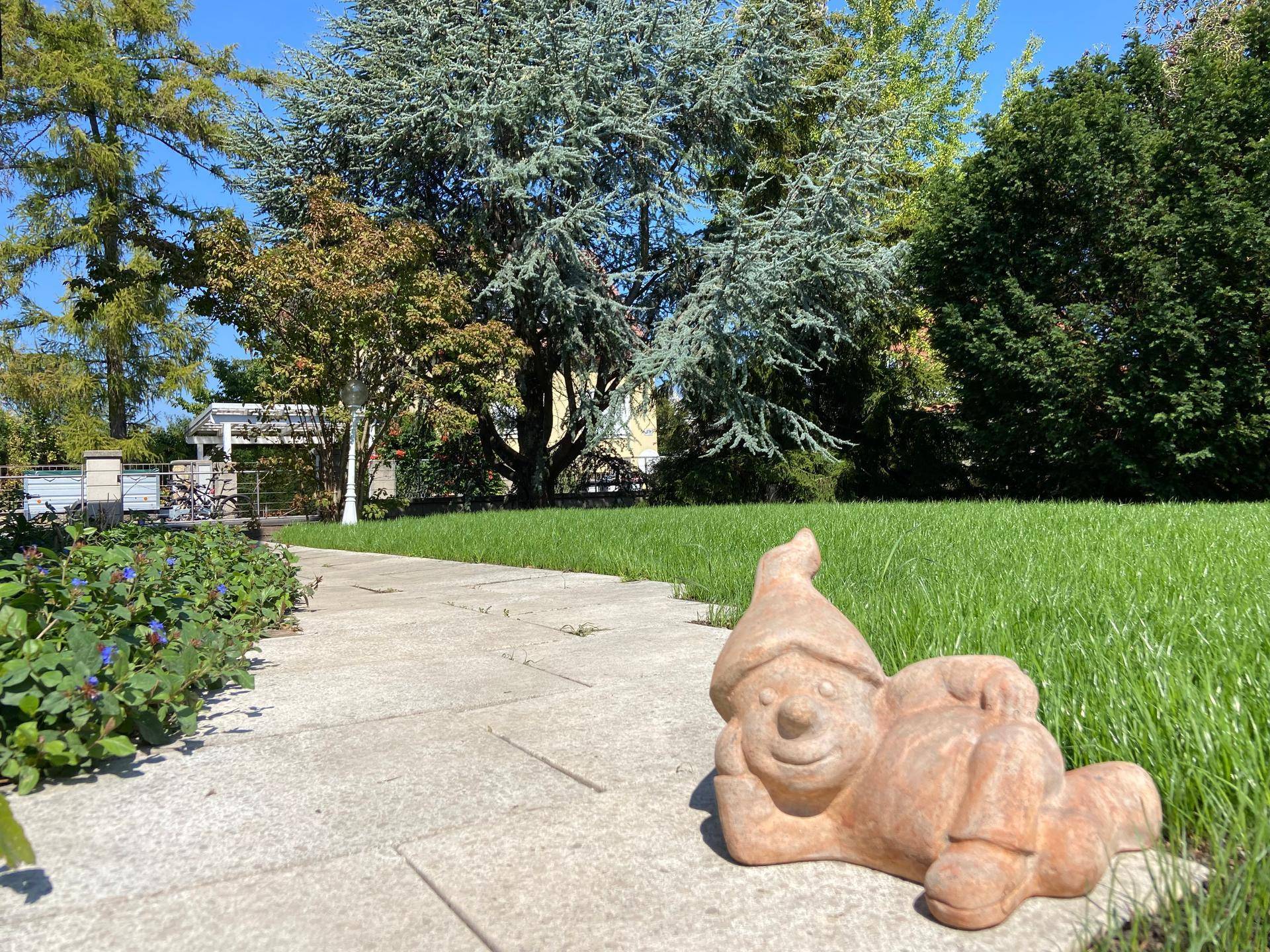 Gartenweg mit einem Gartenzwerg im Vordergrund, der zu einem weitläufigen Rasen führt.