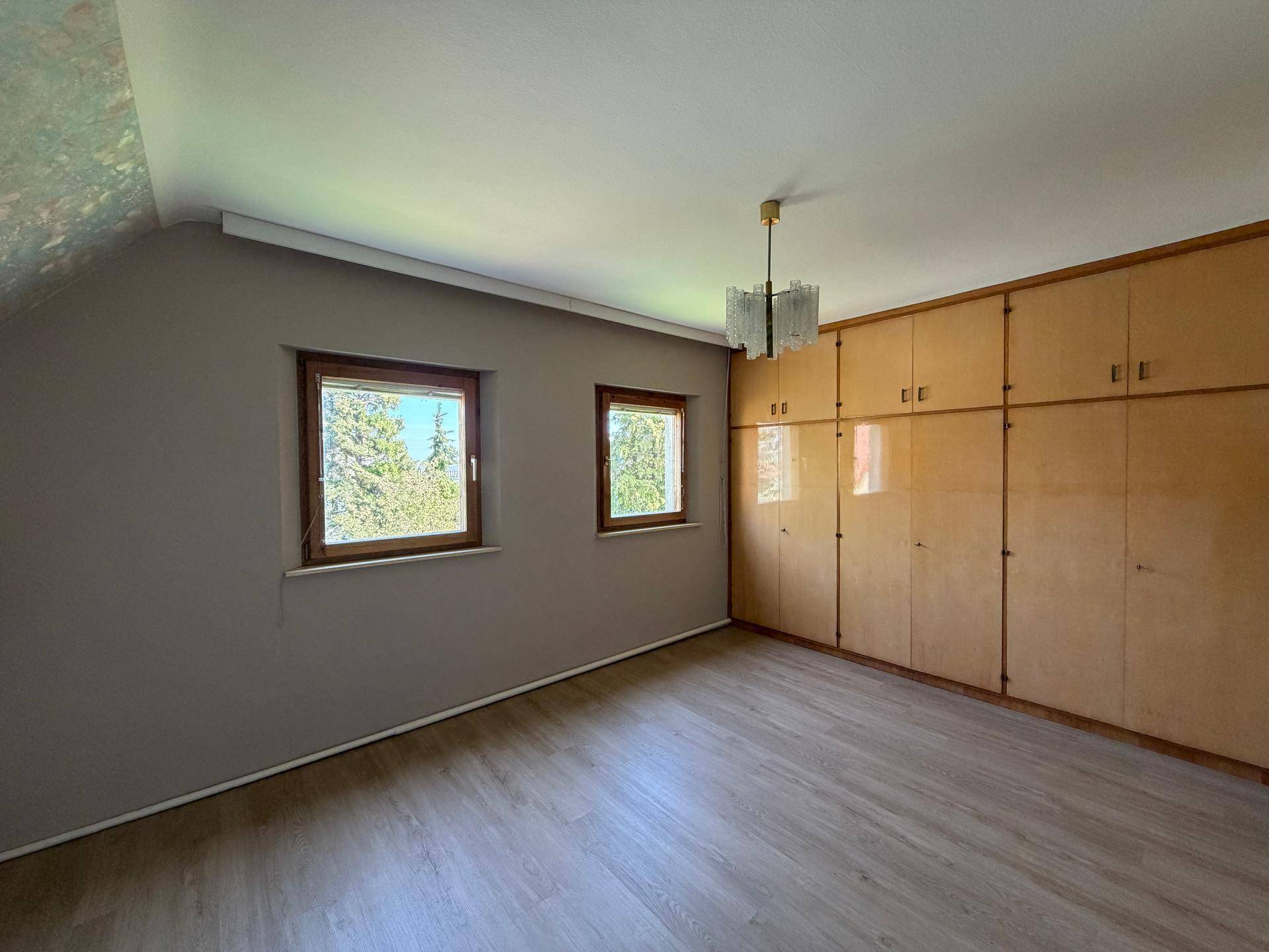 Schlafzimmer mit Einbauschränken aus Holz, zwei Fenstern und Dachschräge.