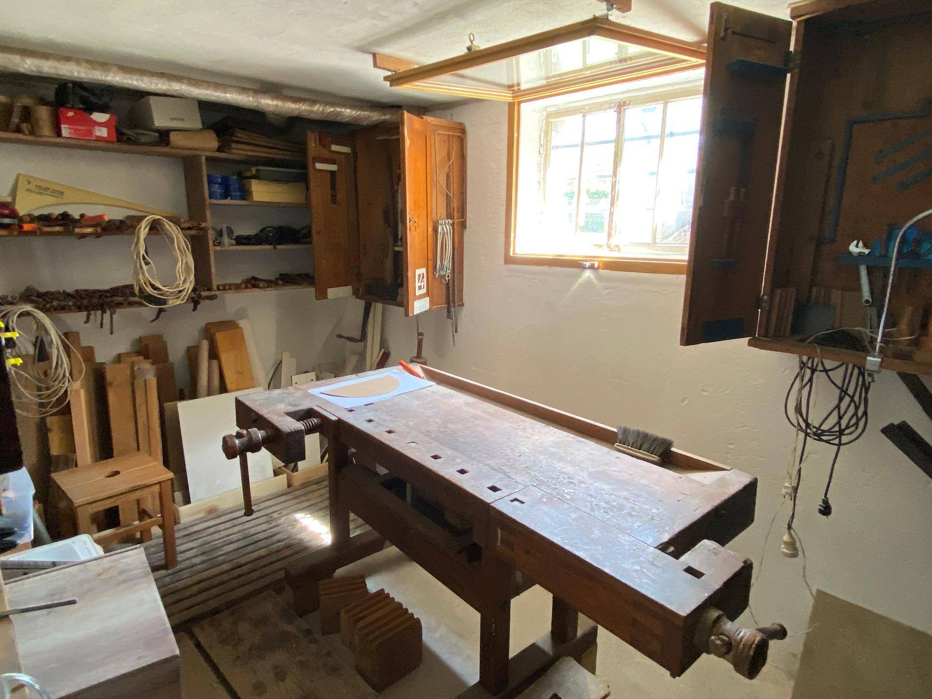Werkstatt oder Hobbyraum mit großer Holzwerkbank, Werkzeugen und Regalen.